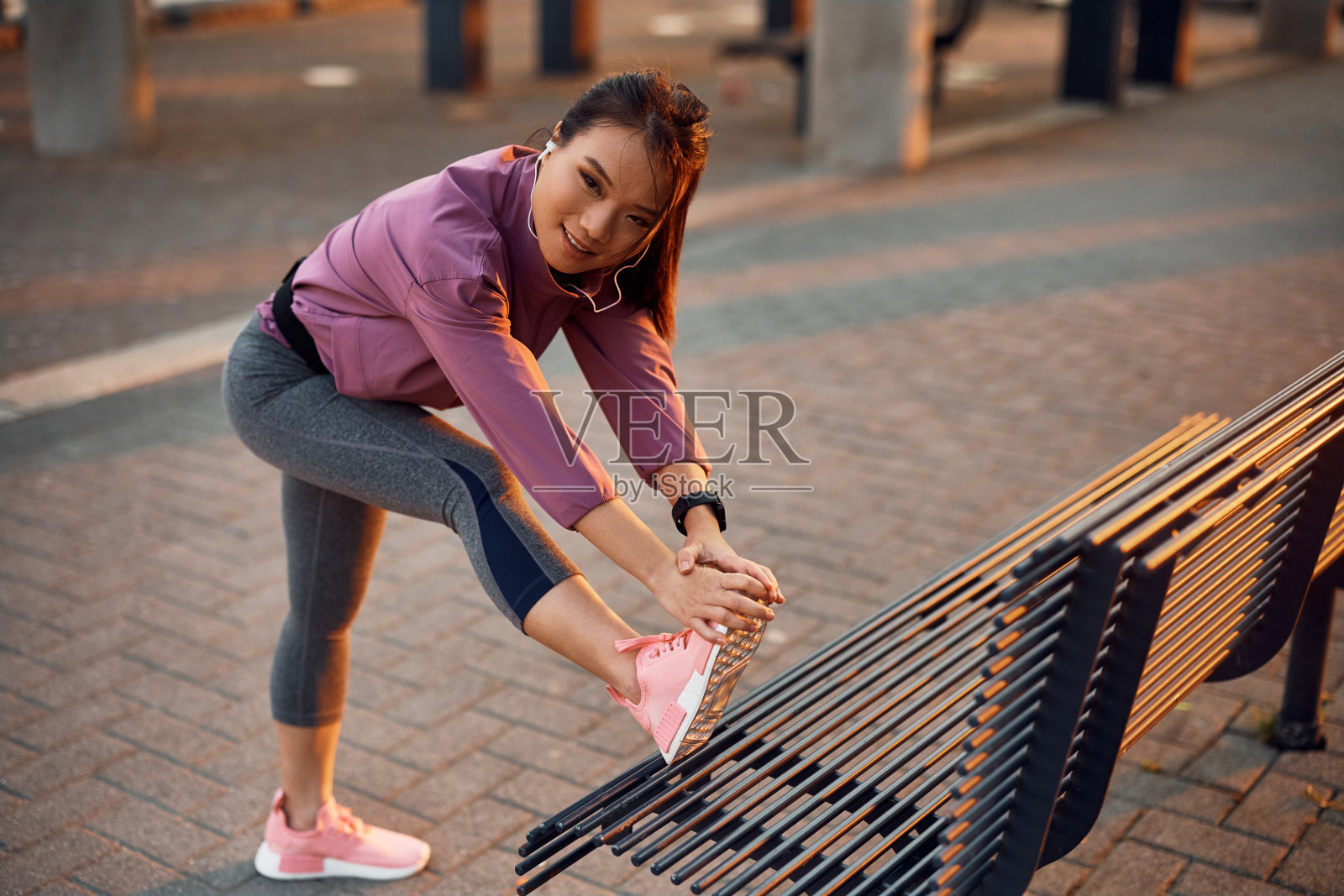 年轻的亚洲运动员在户外热身时伸展她的腿。照片摄影图片