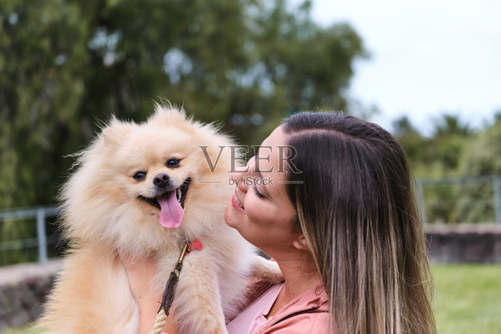 一个女孩的肖像和她的波美拉尼亚狗在公园里。伸出舌头的狗照片摄影图片