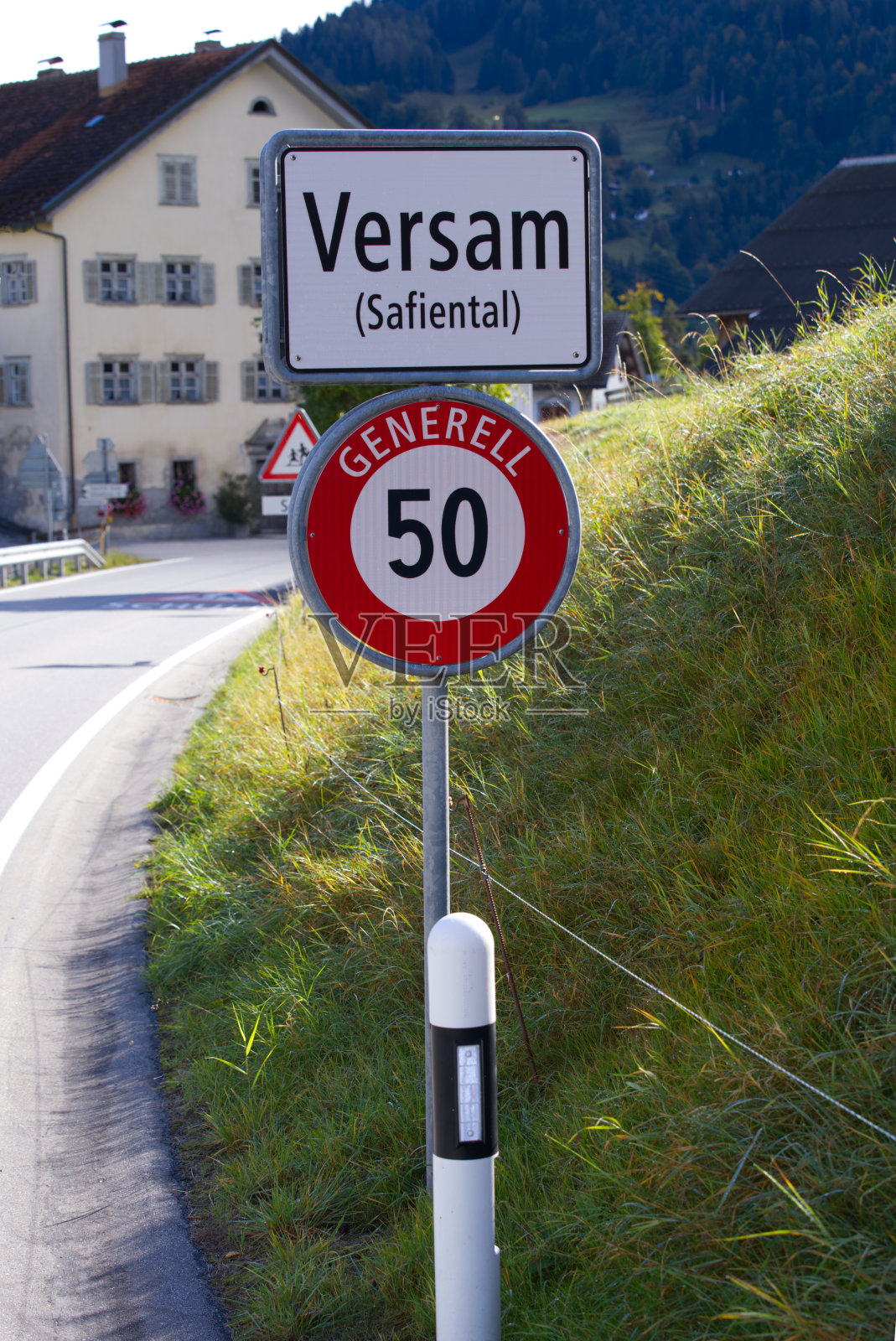 Main road at mountain village Versam, Canton Graubünden, with traffic sign on a blue cloudy autumn day.照片摄影图片
