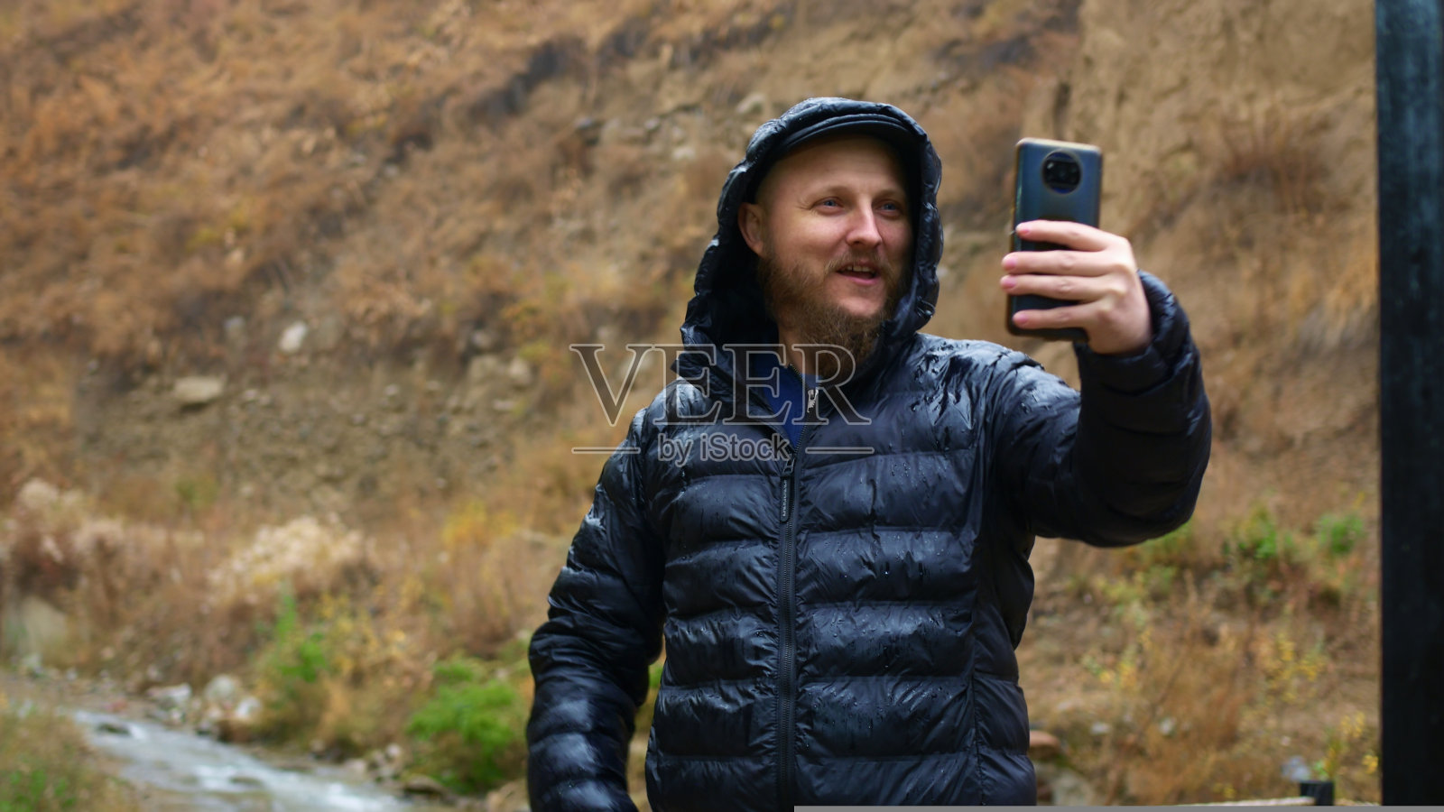 初学者旅行博主正在录制小河流和瀑布之旅的短视频。白人男子兴奋而热情地谈论着美丽的天气和他到达的地区。照片摄影图片