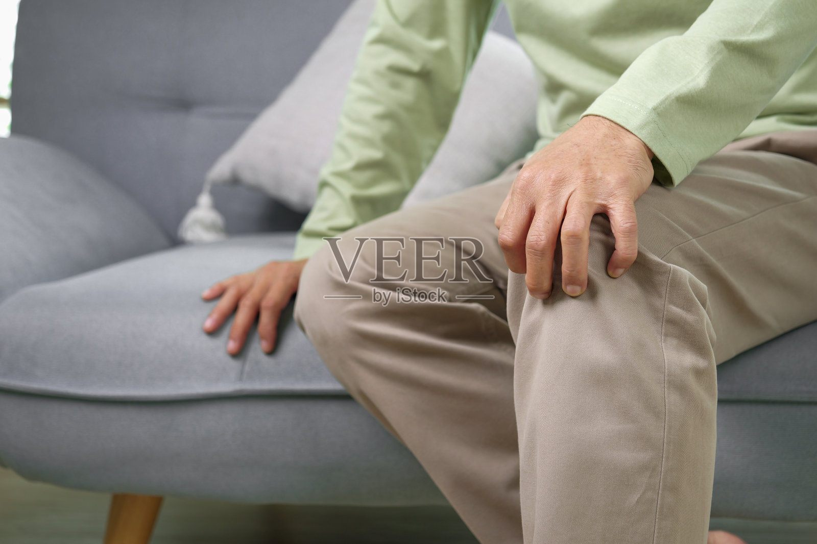 老人用手触摸膝盖痛点,老人坐在家里沙发上忍受膝盖疼痛,有健康问题观念的人照片摄影图片