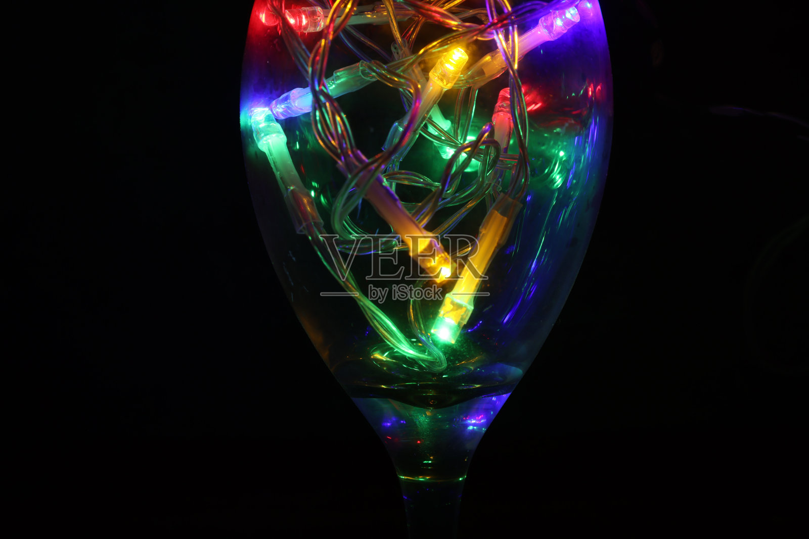 彩色照明在一个葡萄酒杯孤立在黑色背景。照片摄影图片