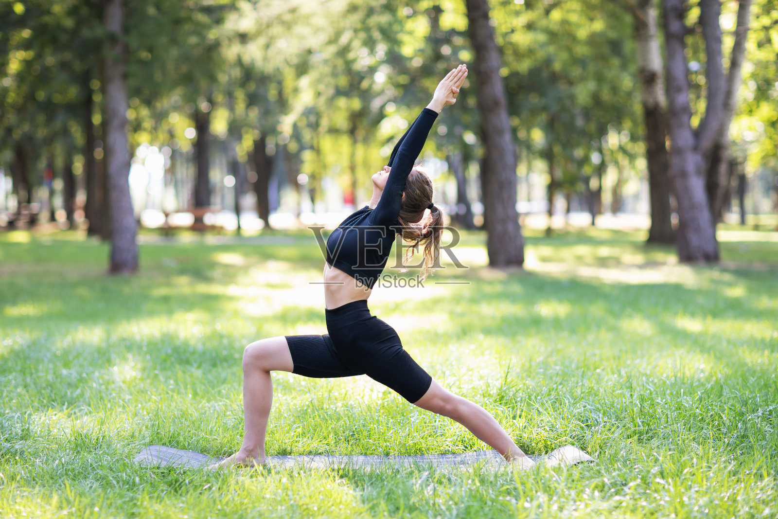 年轻女子过着健康的生活方式,练习瑜伽,进行virabhadrasana练习,战士姿势,独自在一个夏天的早晨在公园的垫子上训练照片摄影图片