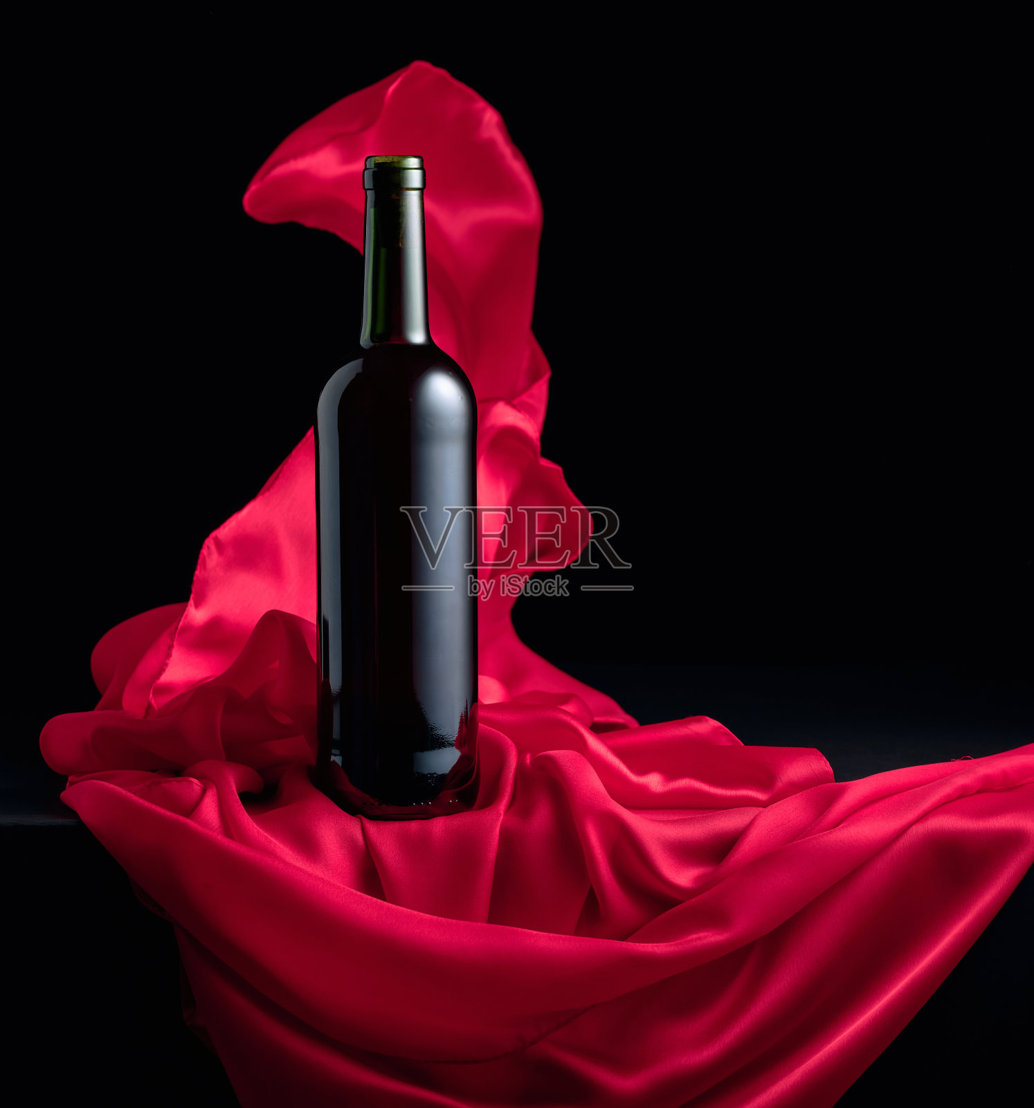 一瓶红酒和飘动的红布。照片摄影图片
