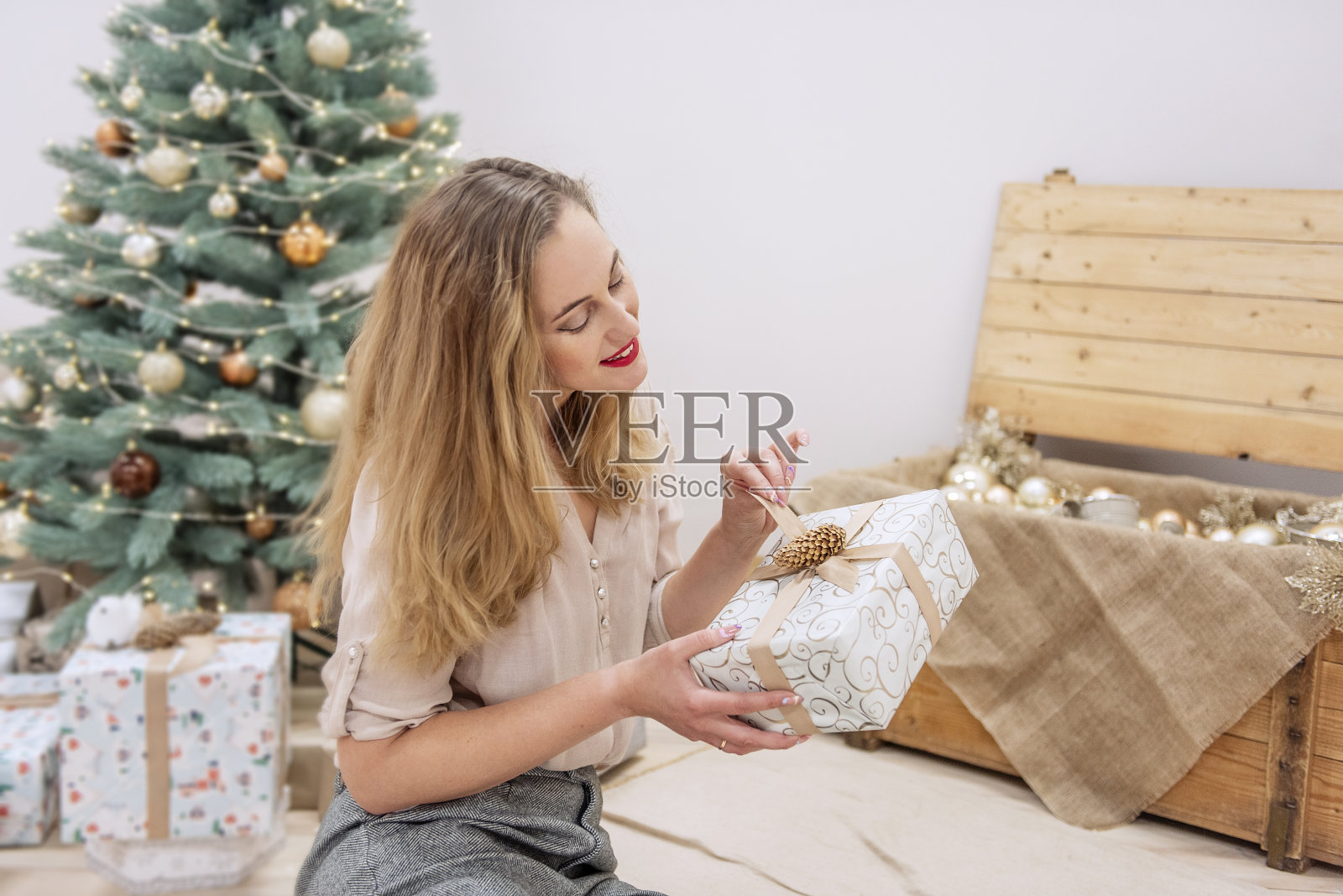时尚、现代的千禧一代女性坐在人造圣诞树前,手里拿着礼物,面带微笑照片摄影图片