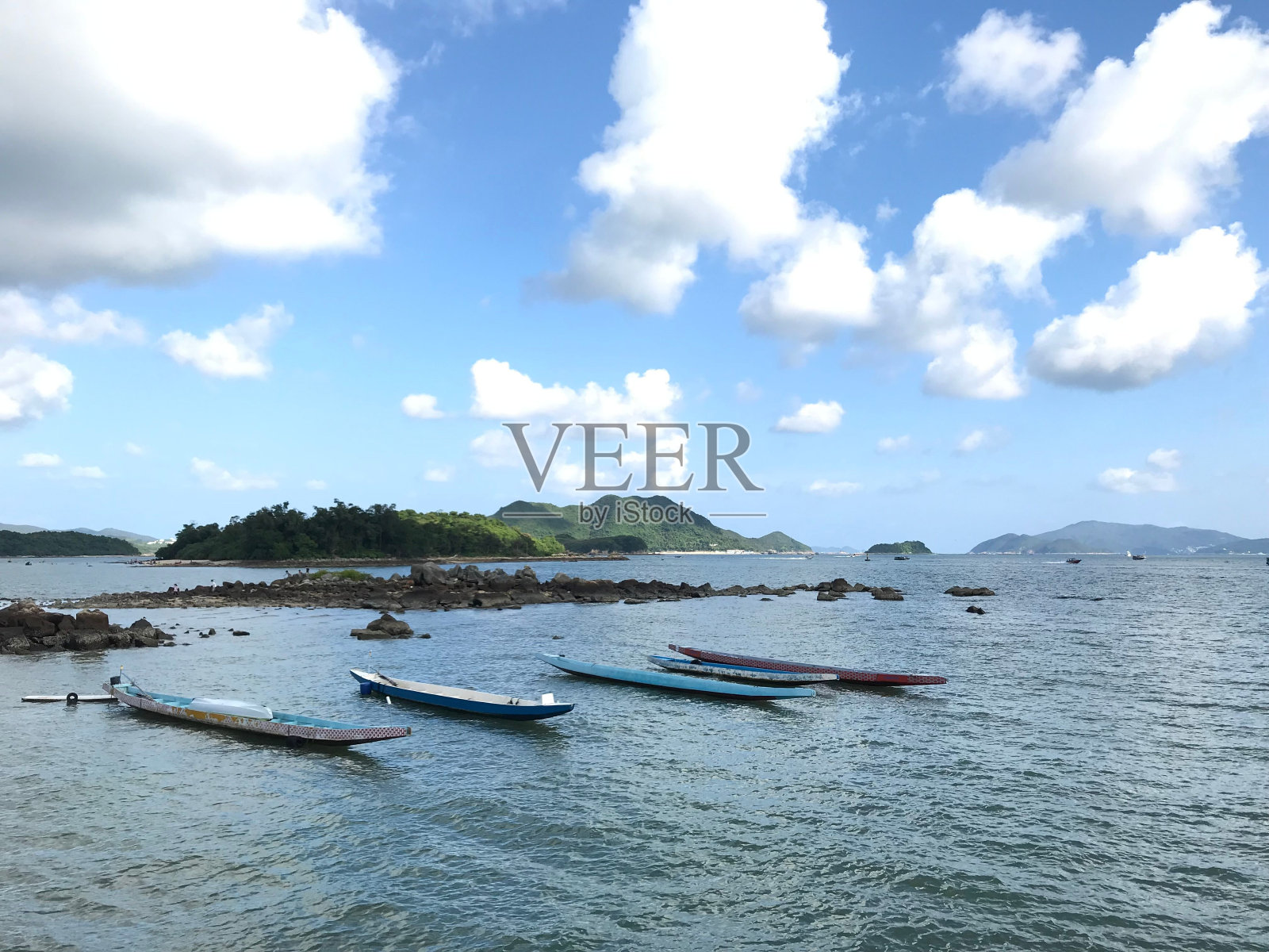 一排长长的划艇在宁静的水面上,四周是绿色的小山,天空是明亮的多云照片摄影图片