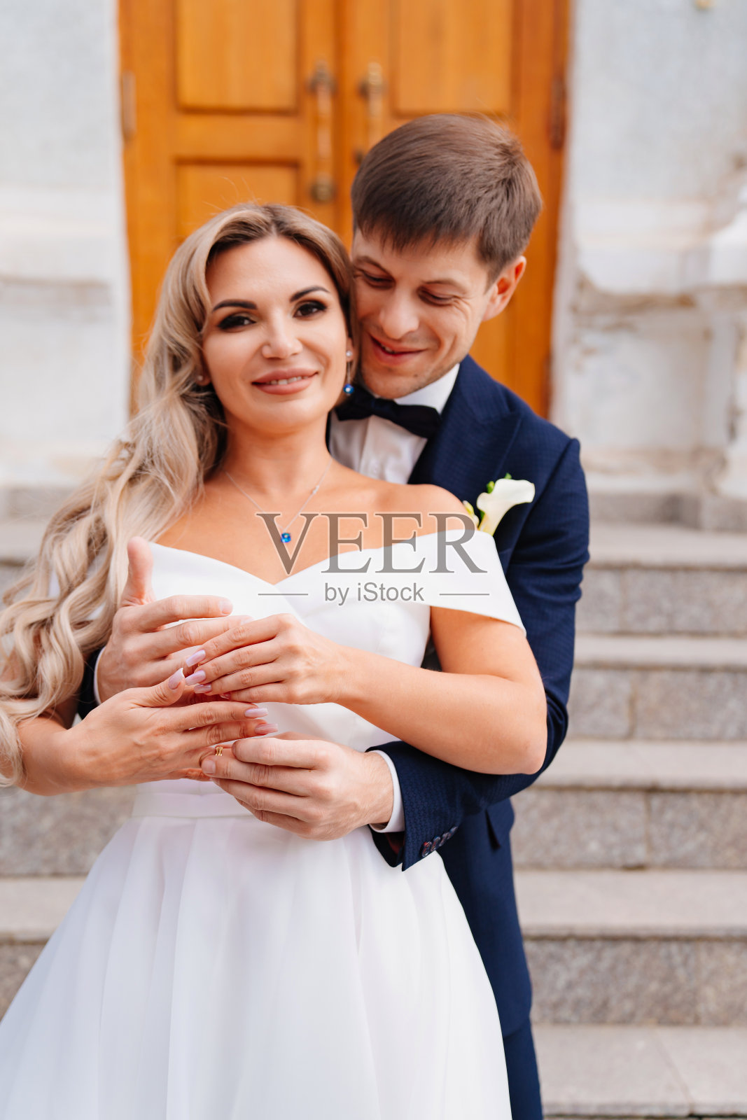 新郎拥抱新娘,他们在大楼的台阶上交换戒指。照片摄影图片