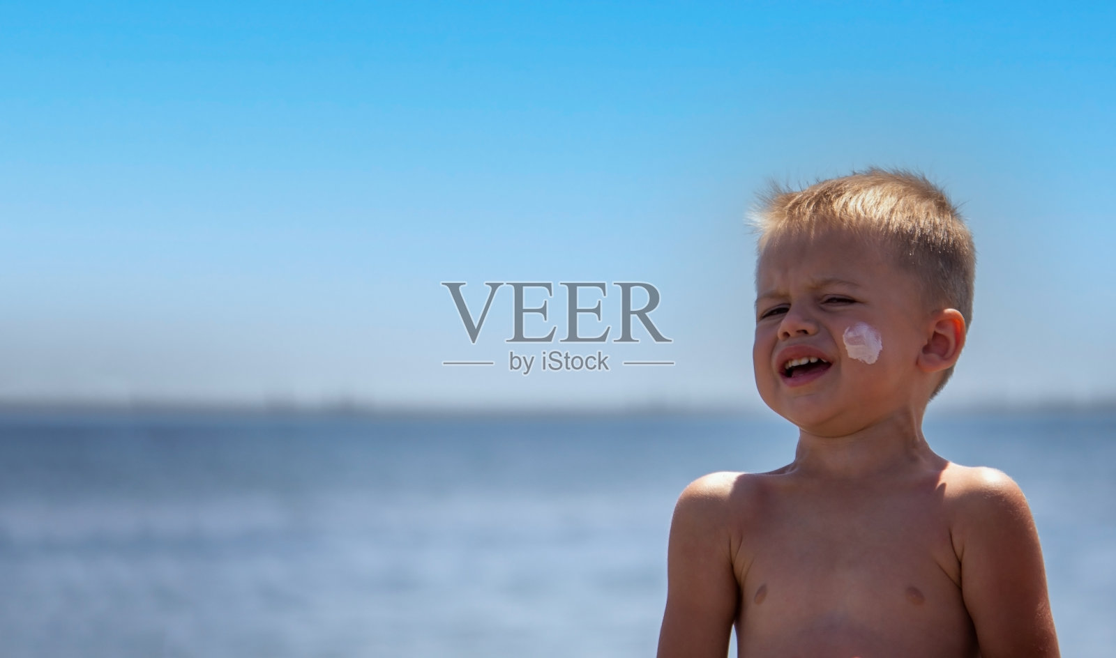 在孩子的脸上和背上涂防晒霜。以大海为背景。照片摄影图片