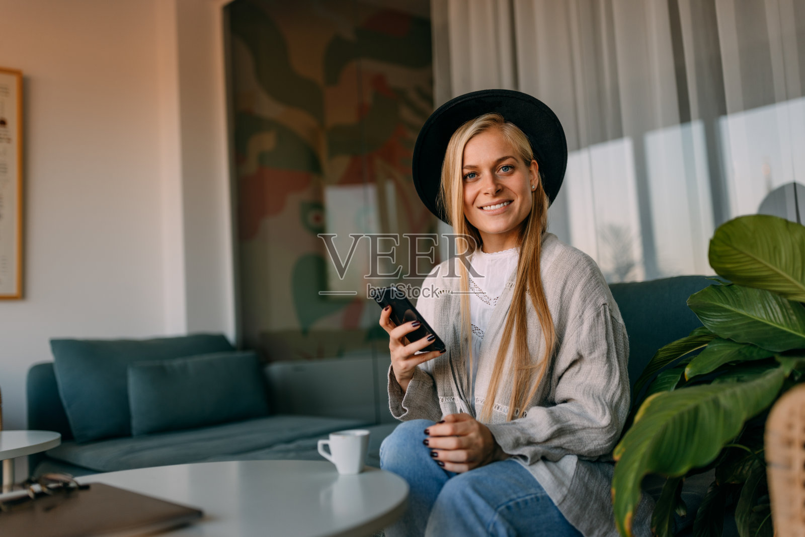 画像上一位面带微笑的女性,戴着帽子,穿着随意,手里拿着手机。照片摄影图片