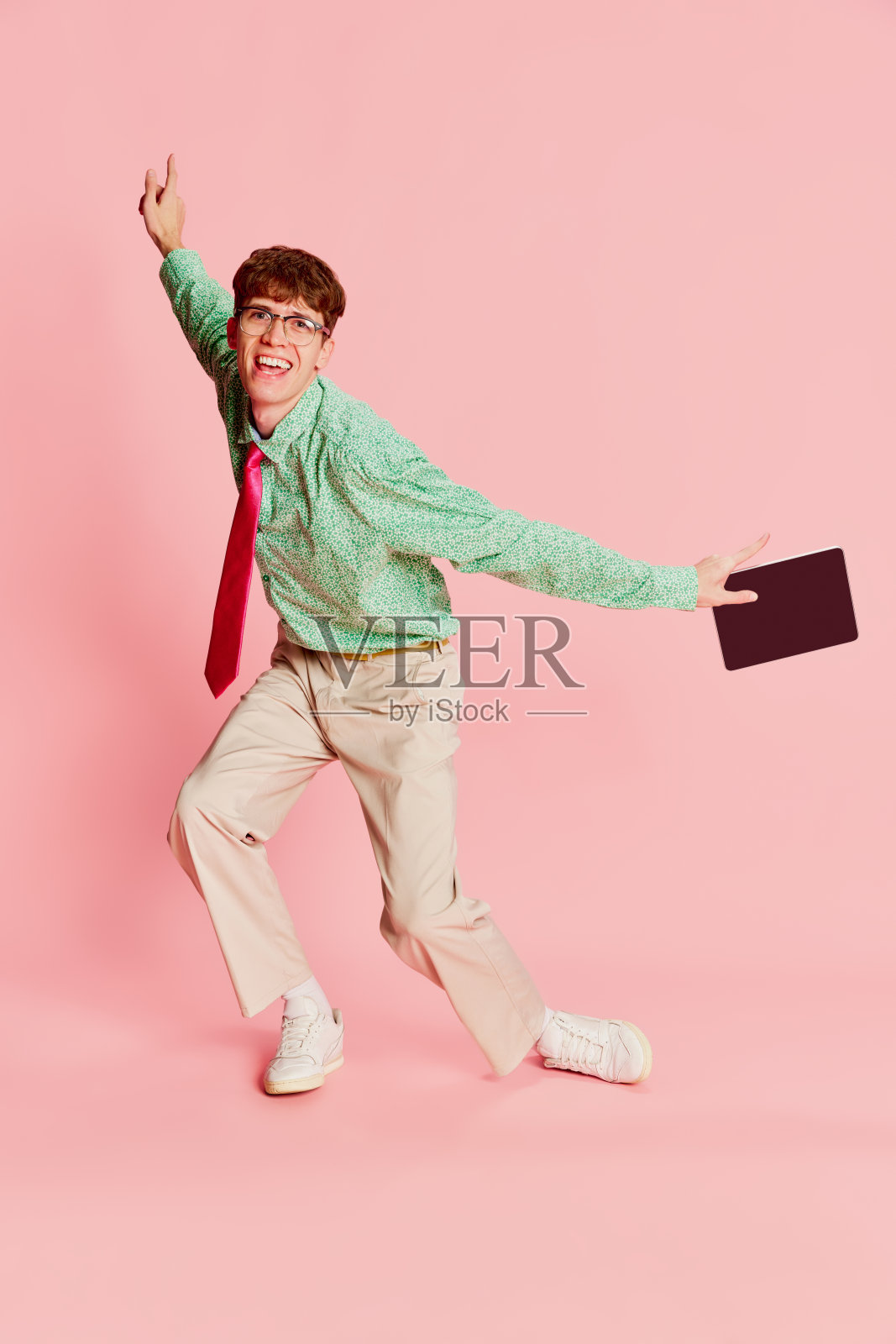 跳舞。时尚感性的男人,学生极客穿着复古风格的衬衫和裤子,在浅粉色背景下摆出孤立的姿势。乐趣,风格,时尚,情感照片摄影图片