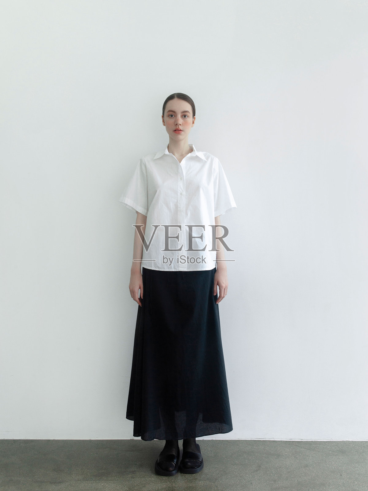 美丽的年轻女子穿着时尚简约的衣服斯堪的纳维亚风格白色短袖衬衫长宽黑色长裙时装模特摆造型看起来富有表现力自信漂亮时装模特工作室肖像在光背景照片摄影图片