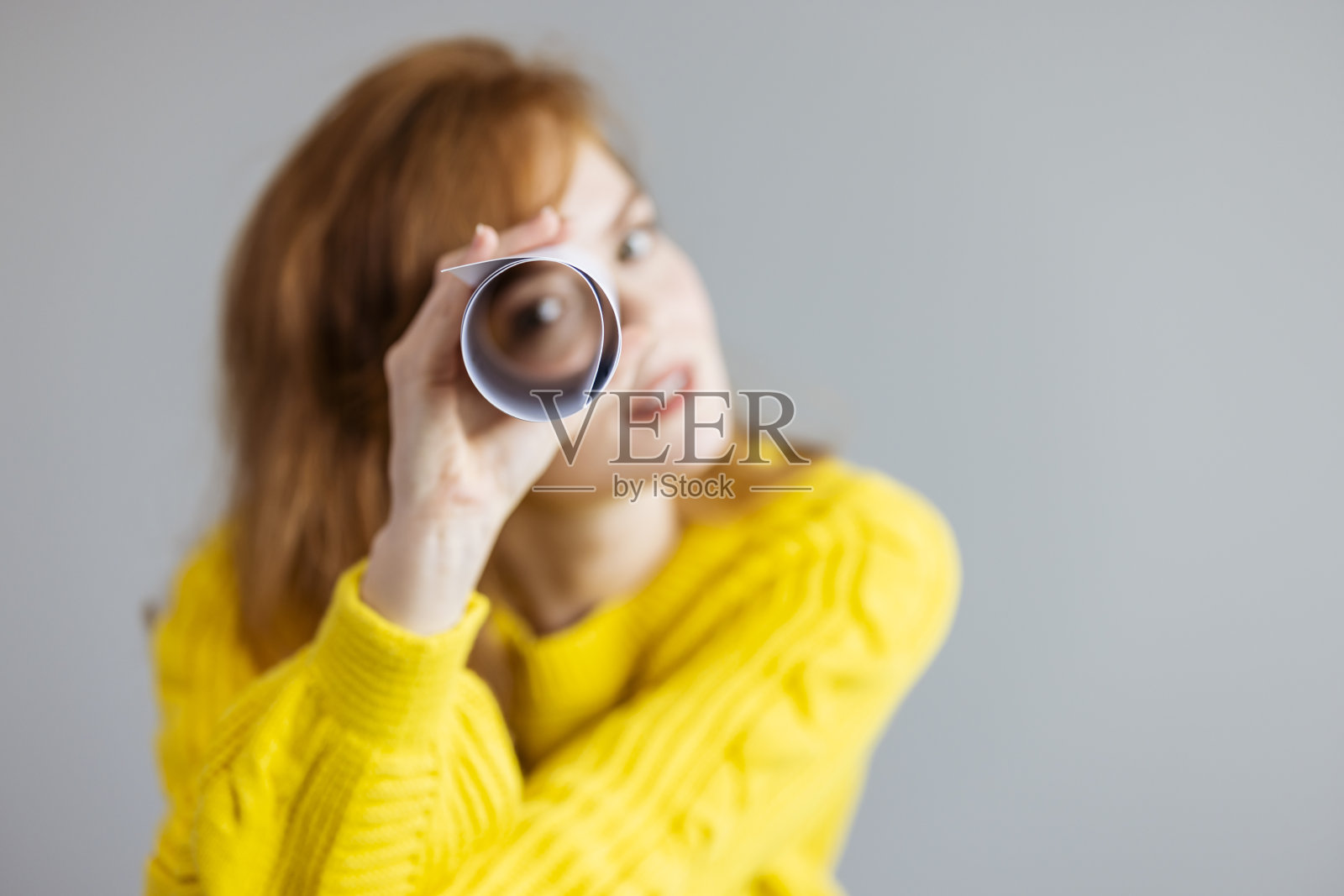 红发女人透过纸望远镜看照片摄影图片