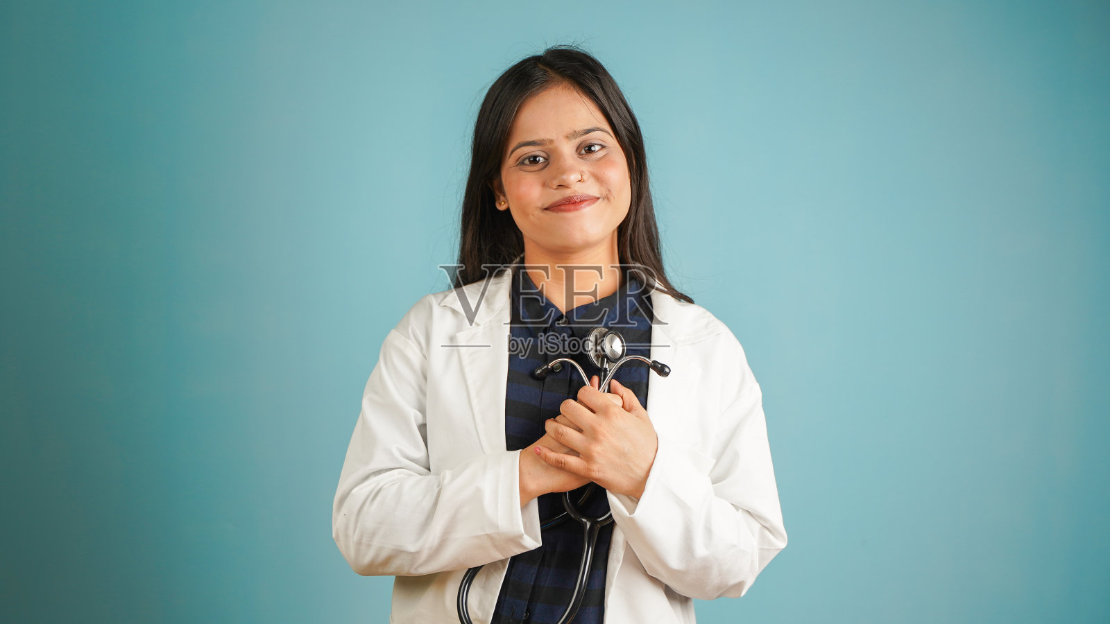 一个年轻的女医生手持听诊器的肖像,开朗的亚裔印度女医生在围裙和听诊器孤立的蓝色工作室背景照片摄影图片
