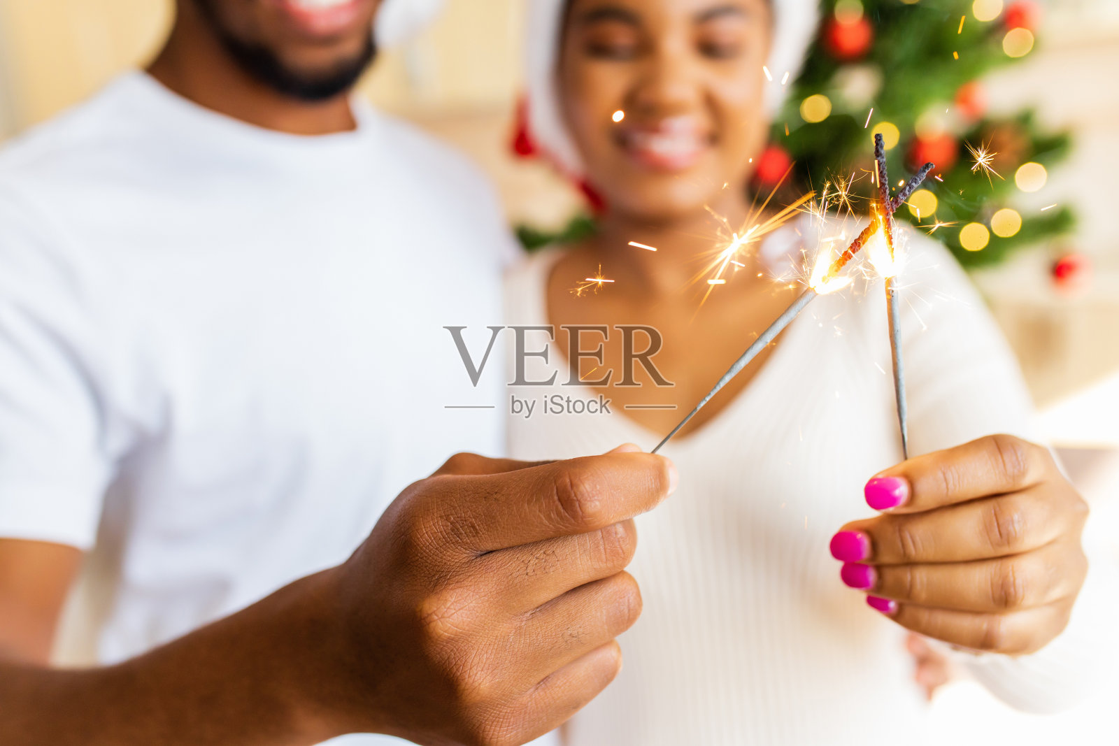 一对拉美裔夫妇在家里的圣诞树旁拿着烟火照片摄影图片