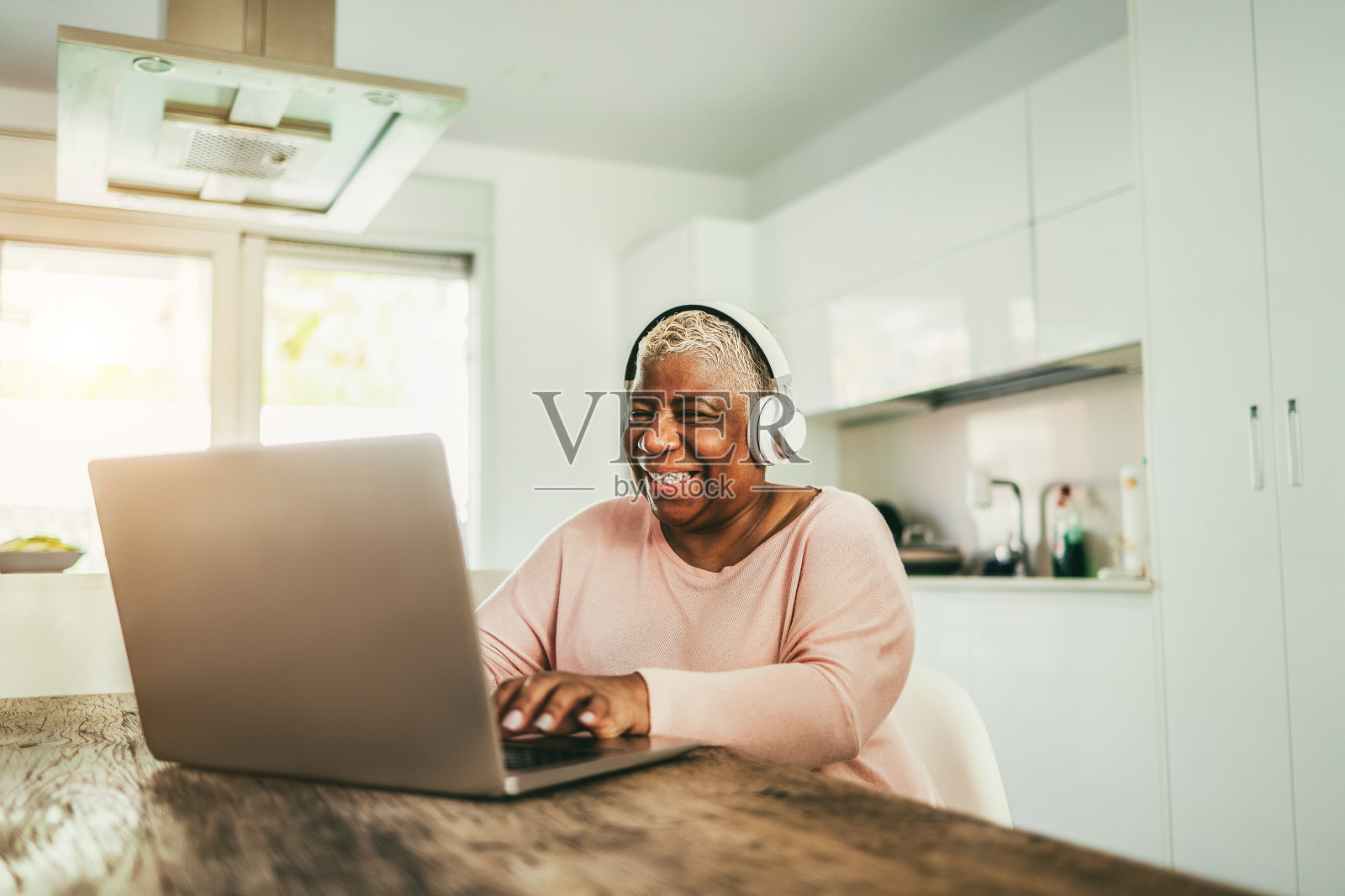 老年妇女在家里戴着耳机使用笔记本电脑-注意面部照片摄影图片