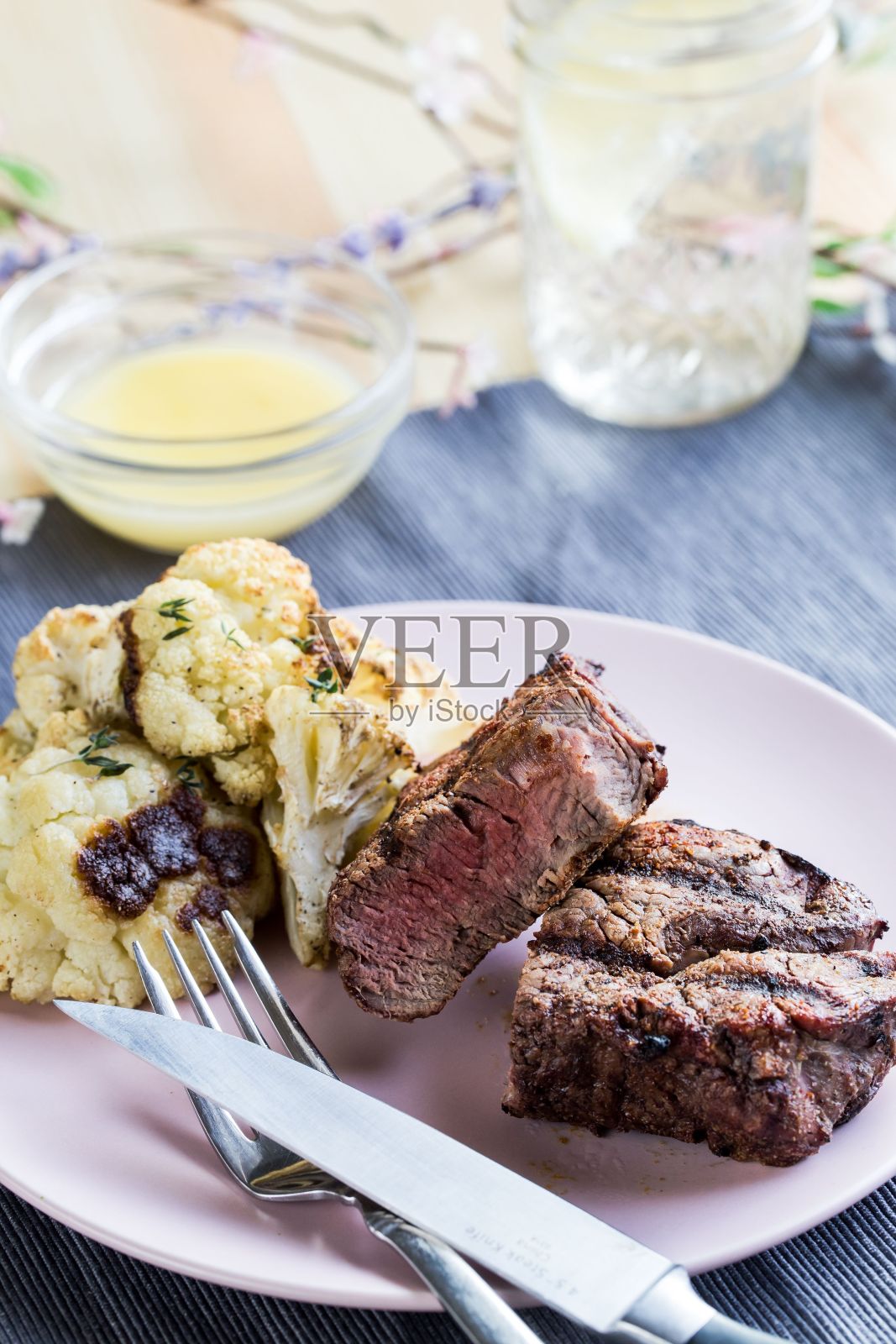 垂直特写镜头的牛排晚餐在一个白色的盘子,酱汁和一杯水照片摄影图片