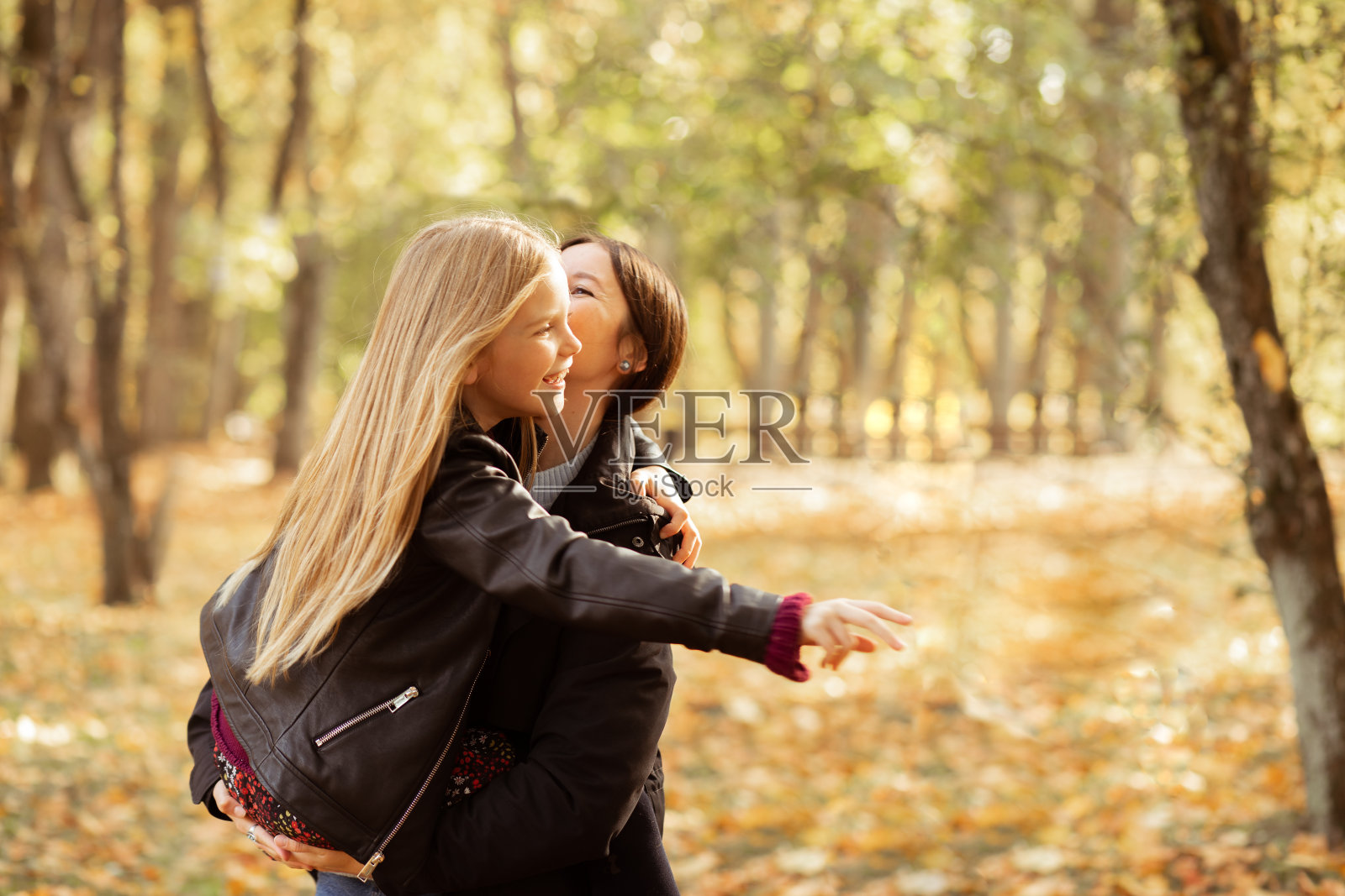 年轻女子和十几岁的女孩站在森林里的家庭肖像。母亲抱着女儿,孩子伸出手。照片摄影图片