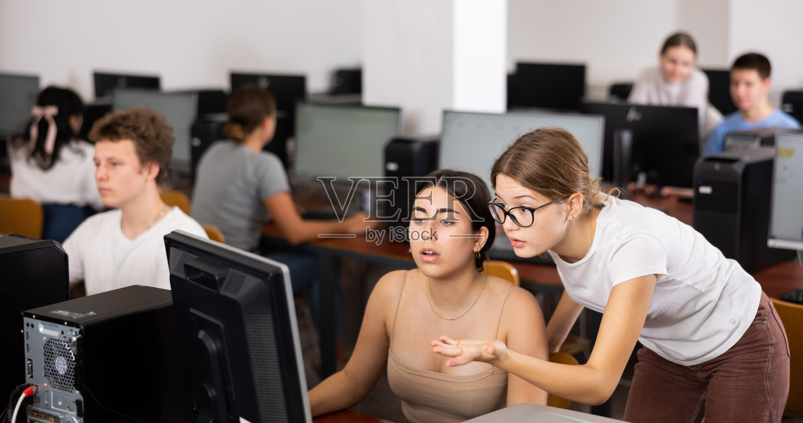 十几岁的女孩在学校课堂上帮助女朋友解决电脑问题照片摄影图片