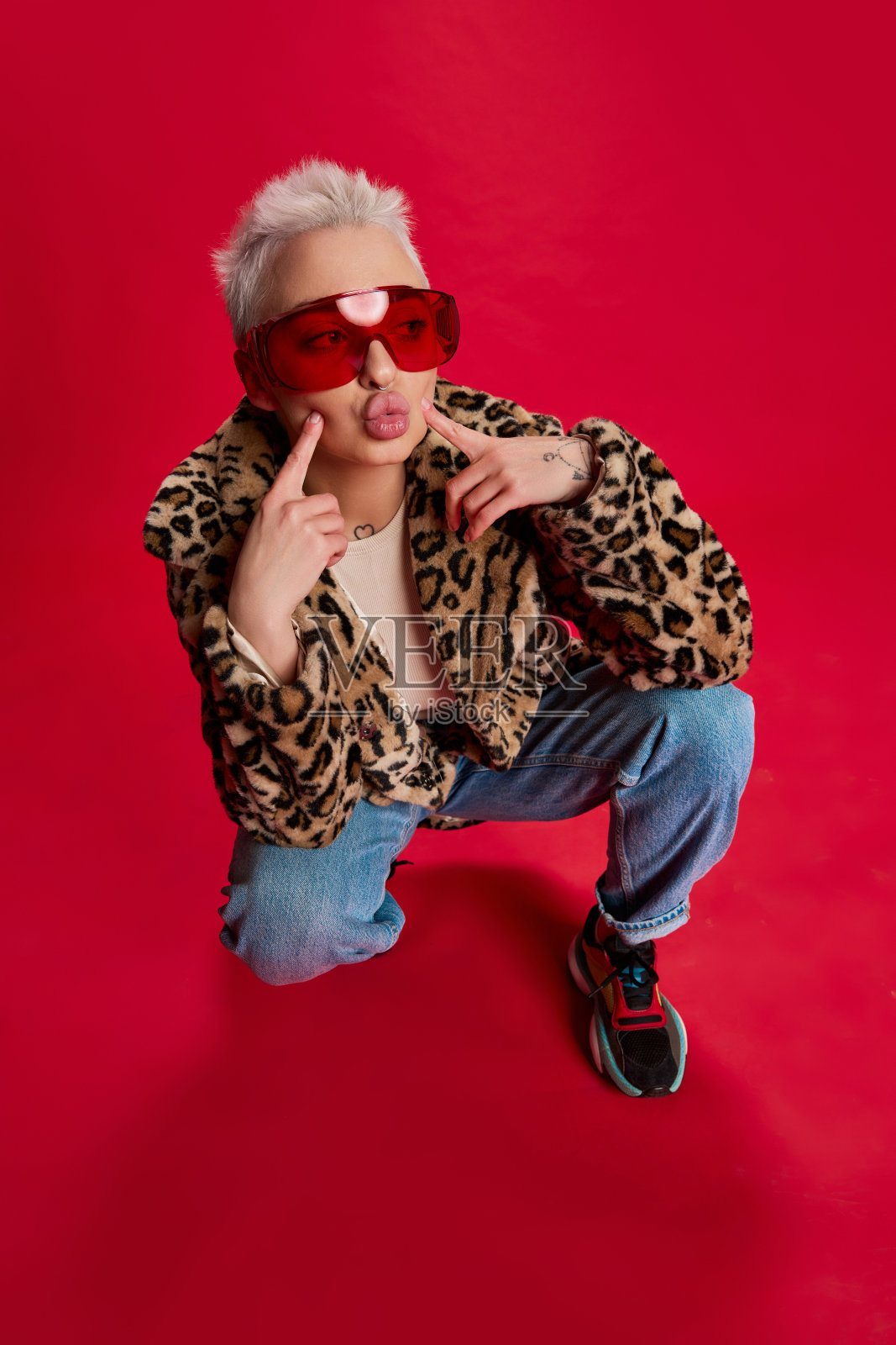 年轻的时尚女子短发摆造型的时尚外套与动物印花孤立在红色背景。安慰照片摄影图片