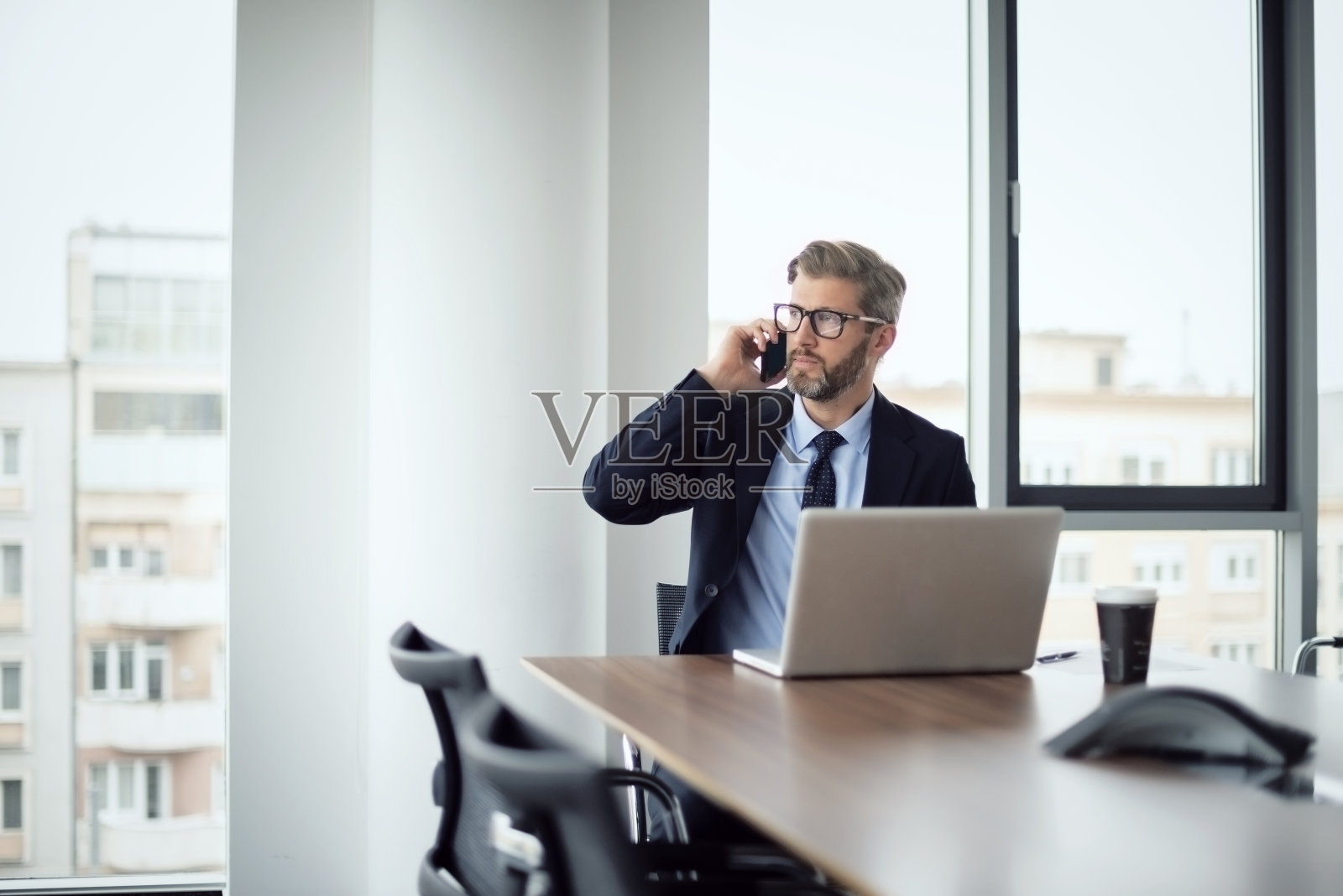 在办公室工作时,正在接听电话并使用笔记本电脑的中年高级商人照片摄影图片