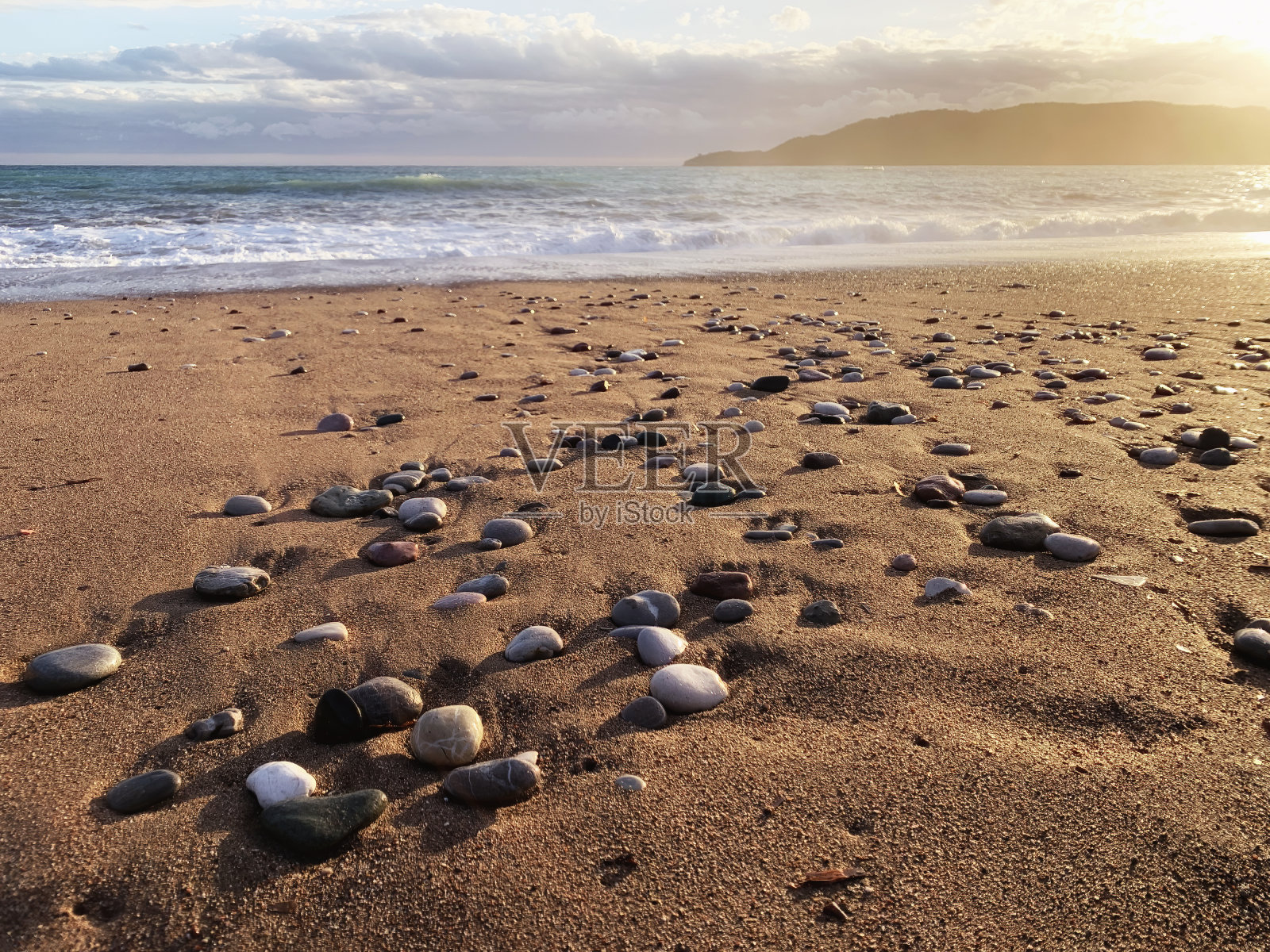 美丽的夕阳照耀着大海和海岸线上的沙子和湿卵石照片摄影图片