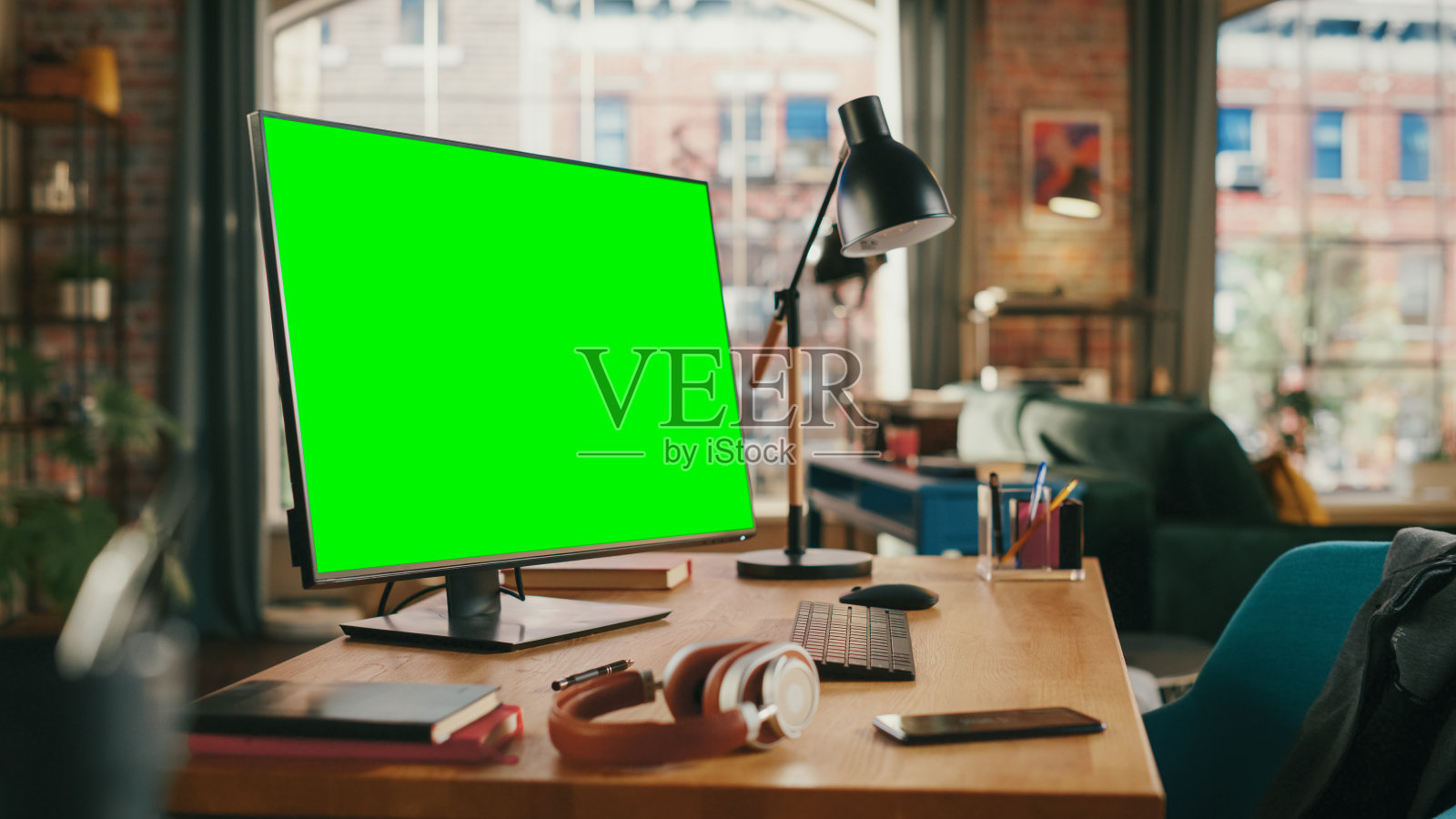 台式电脑与模拟绿色屏幕显示站在书桌上在舒适的客厅。在背景时尚现代明亮的家庭办公工作室在白天与大城市景观窗口。照片摄影图片