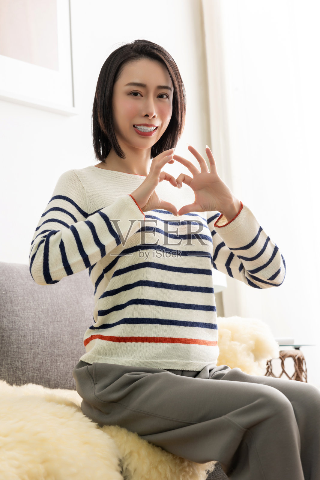 年轻漂亮的亚洲女人坐在客厅舒适的沙发上。照片摄影图片