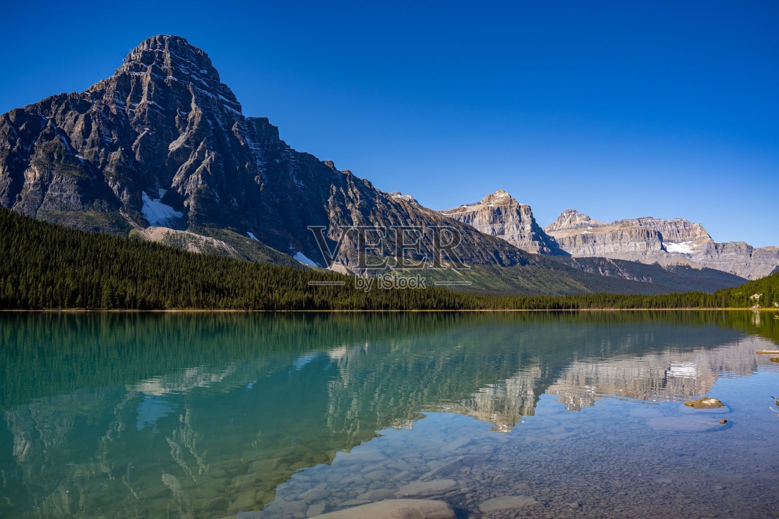 一个透明的山湖表面,背景是森林和雪山斜坡照片摄影图片