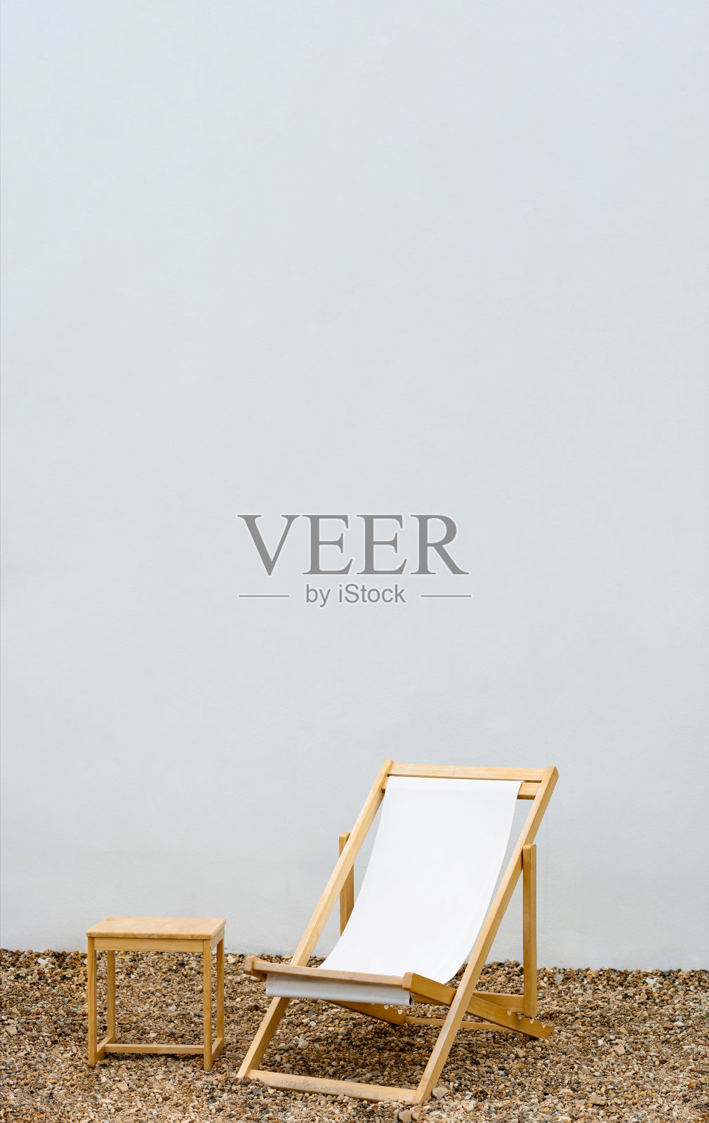 沙滩椅在卵石与白色混凝土墙背景,吊床椅与木桌在白色油漆水泥背景,垂直横幅与复制空间文本春夏假期概念照片摄影图片