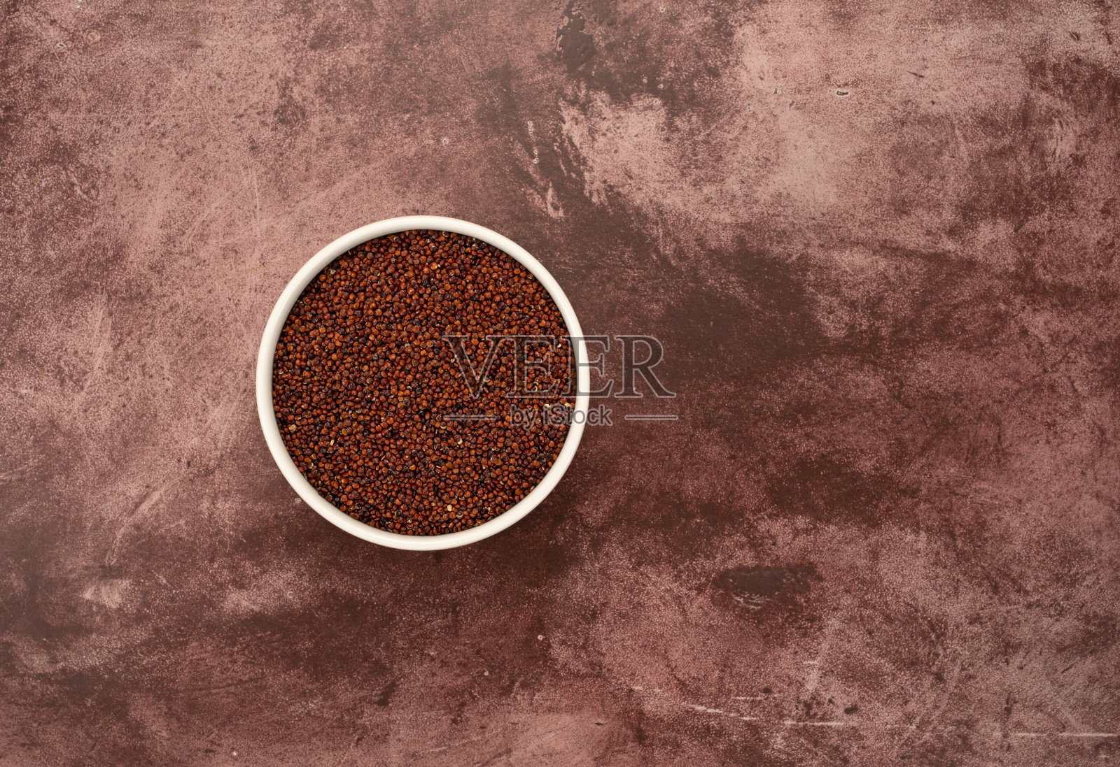 顶部视图的一个白色碗装满红色藜麦抵消在一个栗色的桌面。照片摄影图片