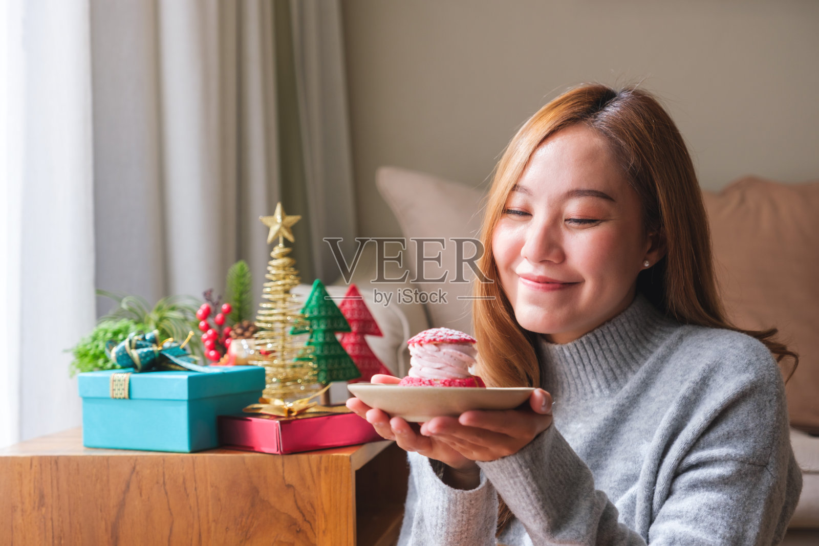 肖像图像的年轻女子在毛衣拿着泡芙蛋糕与圣诞节的节日装饰在家里照片摄影图片