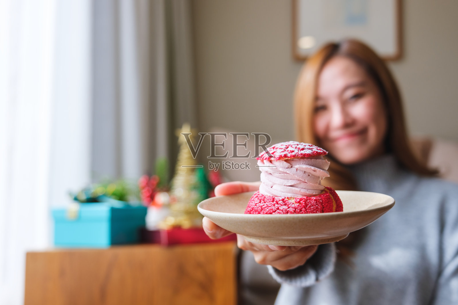 模糊的图像,一个年轻的女人在毛衣和给泡芙蛋糕与圣诞节的节日装饰在家里照片摄影图片