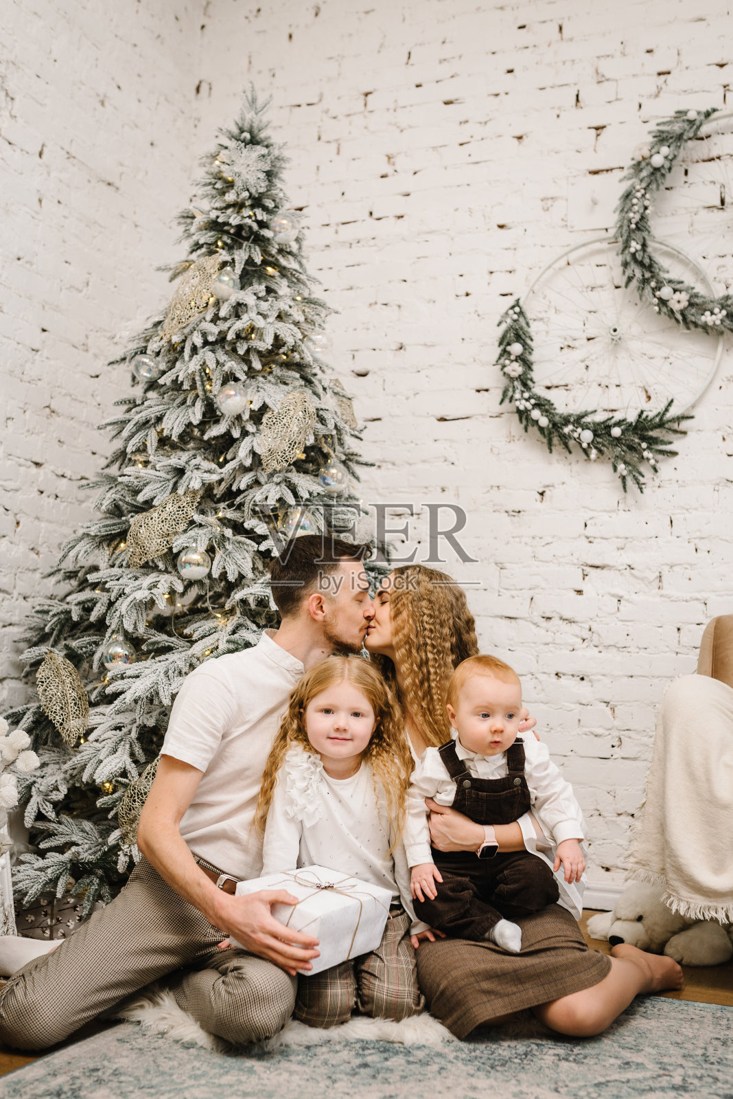 圣诞快乐。快乐的妈妈,爸爸和孩子们在家里的圣诞树旁。妈妈、爸爸拥抱孩子。美丽的家庭一起享受他们的节日时光,玩得很开心。装饰室内:装饰过的房子内部照片摄影图片