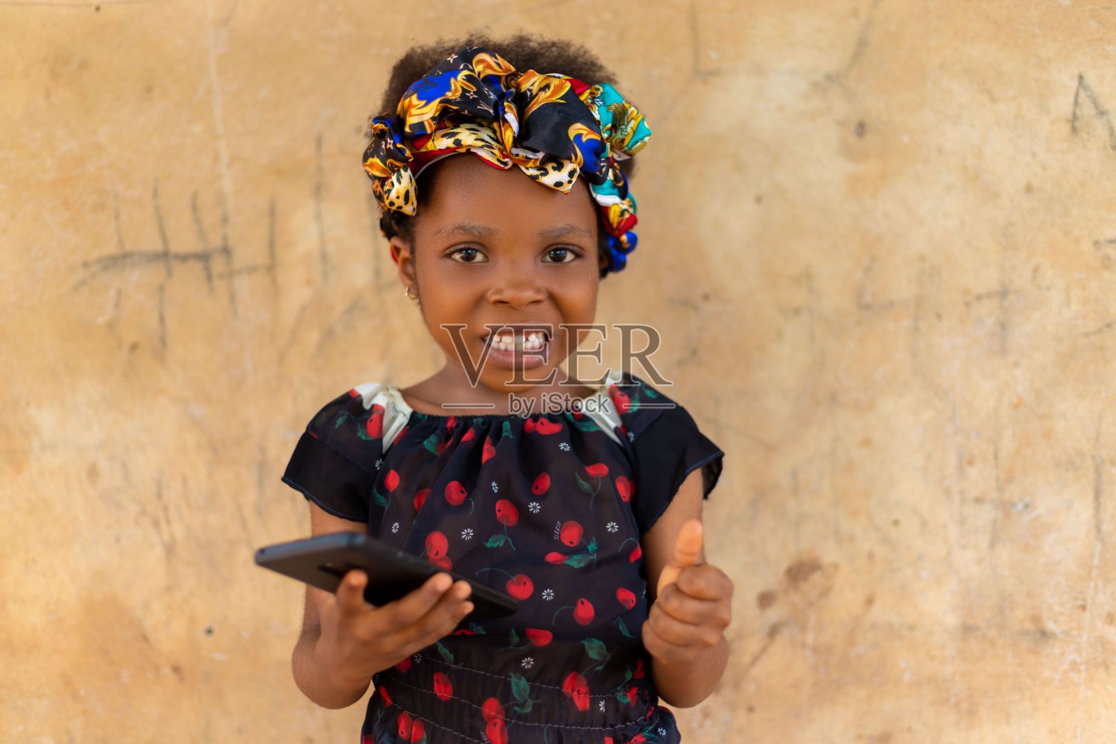 可爱的尼日利亚孩子,带着彩色发带,拿着手机看着相机照片摄影图片