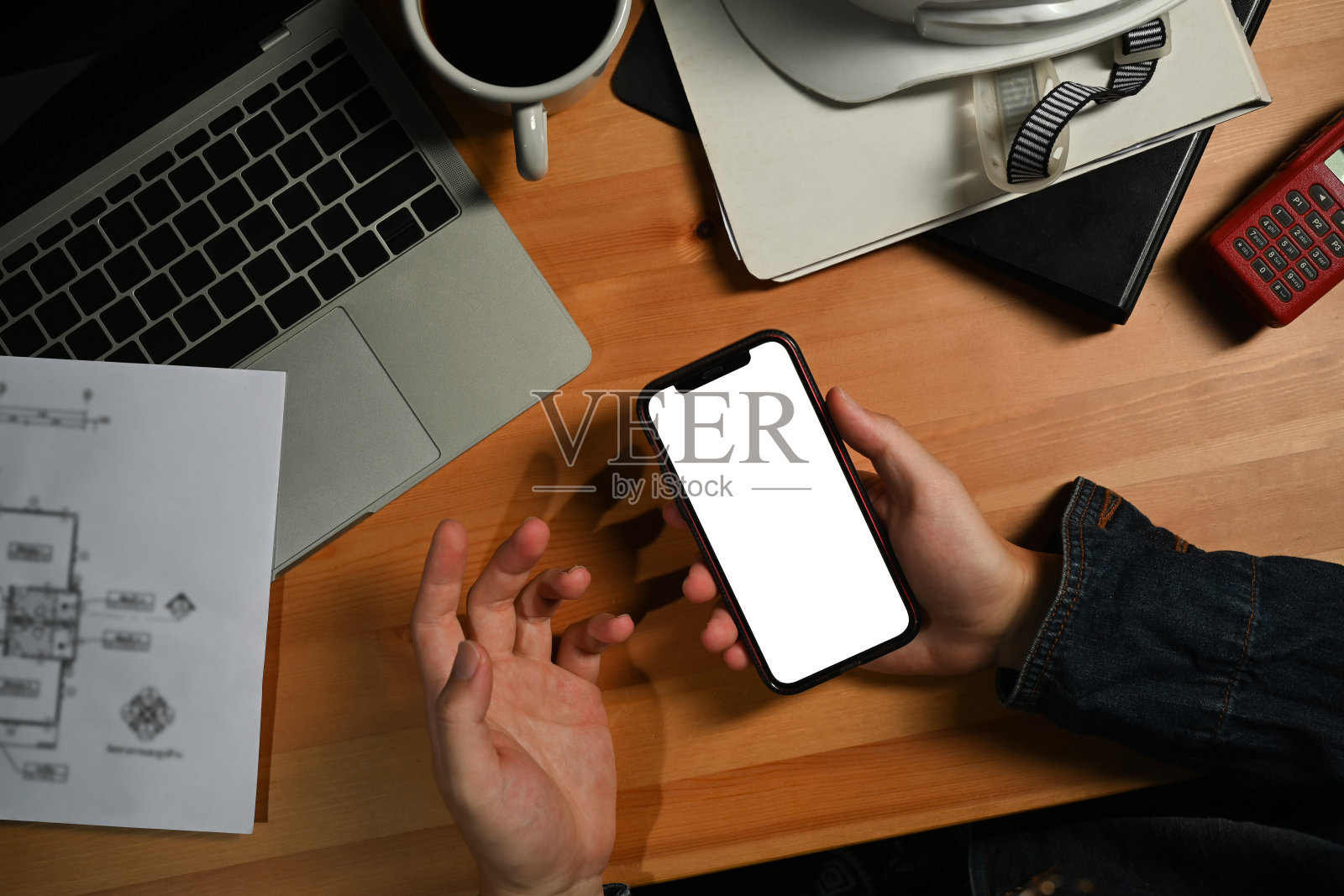 以上视图的工程师男子手拿智能手机在他的工作站。空白屏幕为您的广告。照片摄影图片