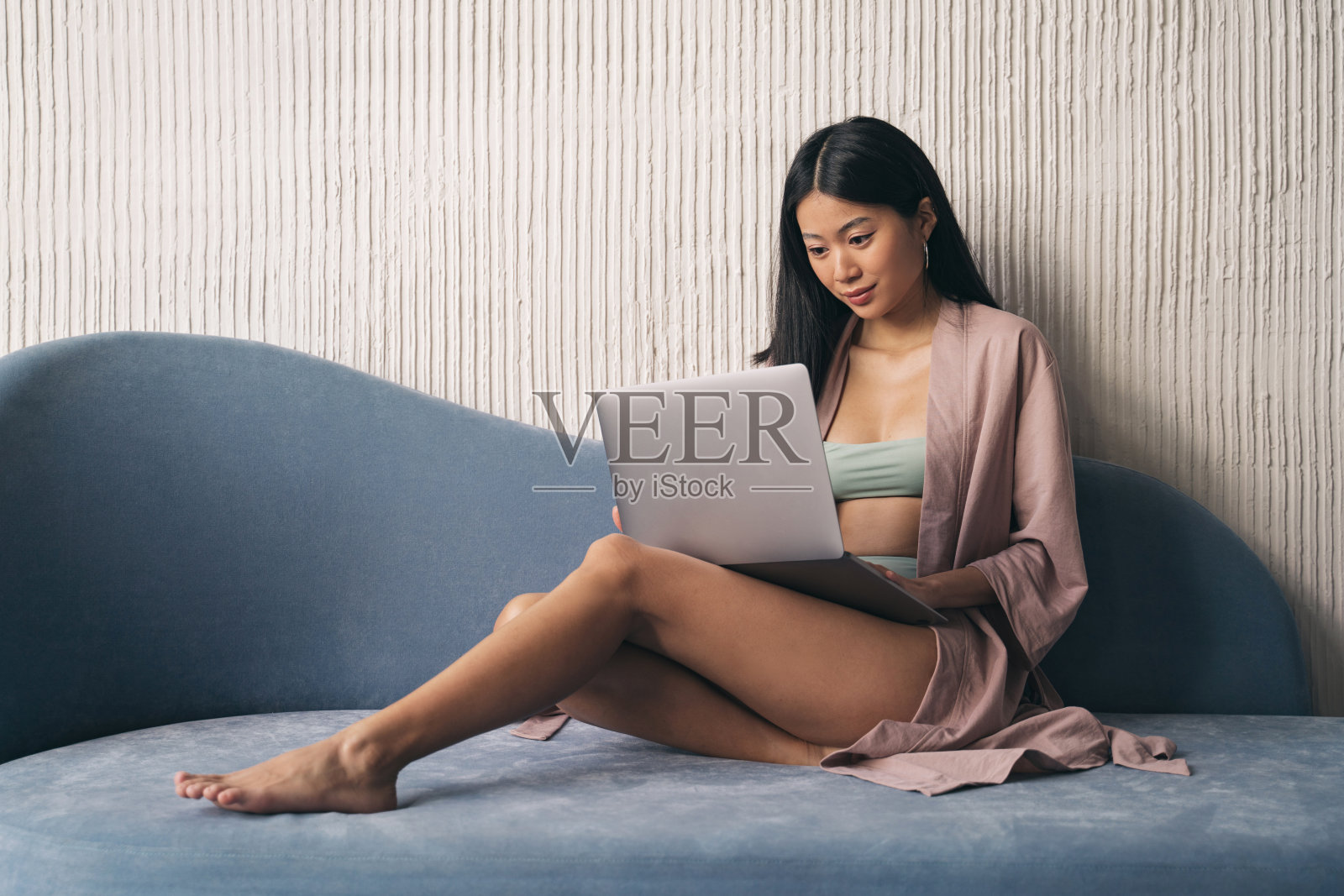 亚洲女人早上坐在沙发上,在家里的笔记本电脑上对着纹理墙工作照片摄影图片