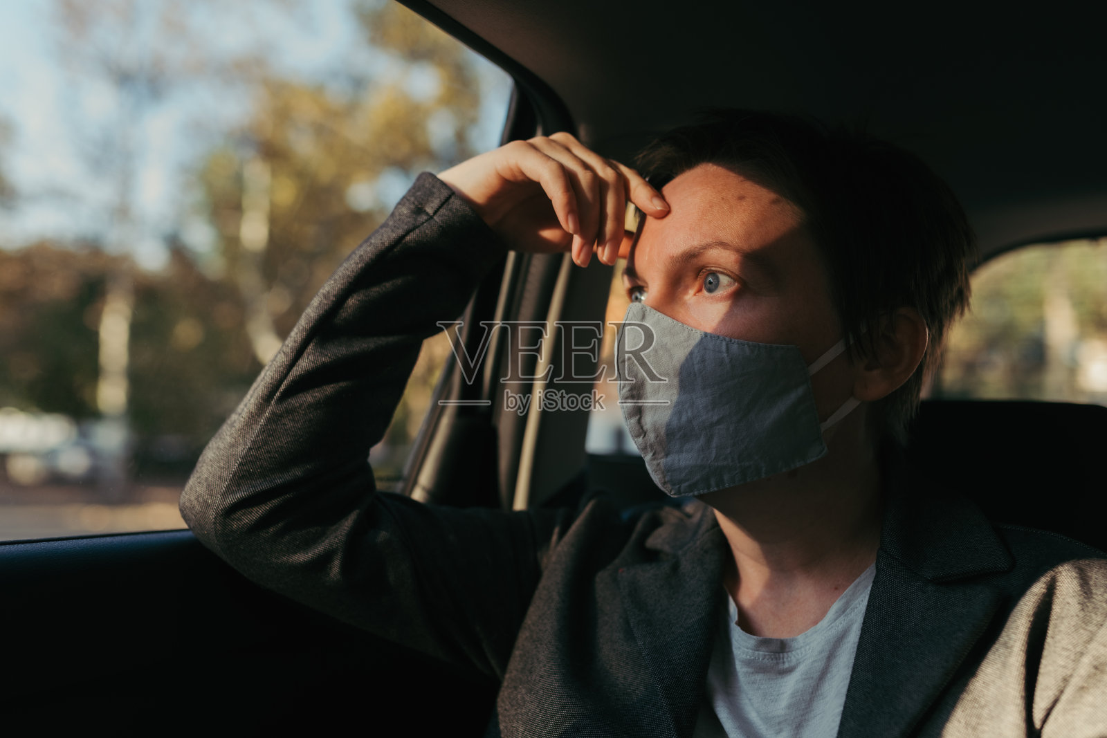忧心忡忡的女商人戴着防护口罩等在车里,看着窗外照片摄影图片