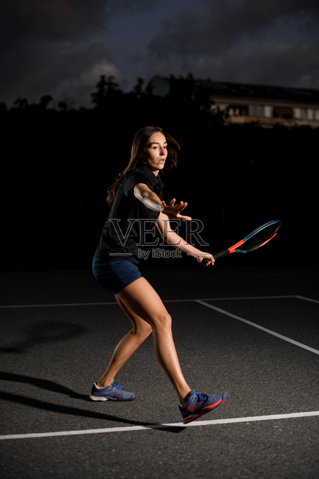 职业女子网球运动员在网球场上,手里拿着球拍。暗的背景照片摄影图片