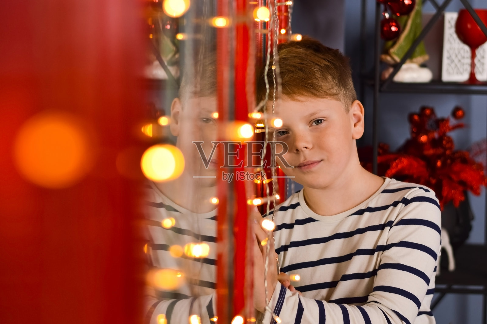 平安夜,一个男孩在家里一间装饰舒适的房间里,手拿花环站在窗前等待圣诞老人的到来。就在奇迹发生前不久。照片摄影图片