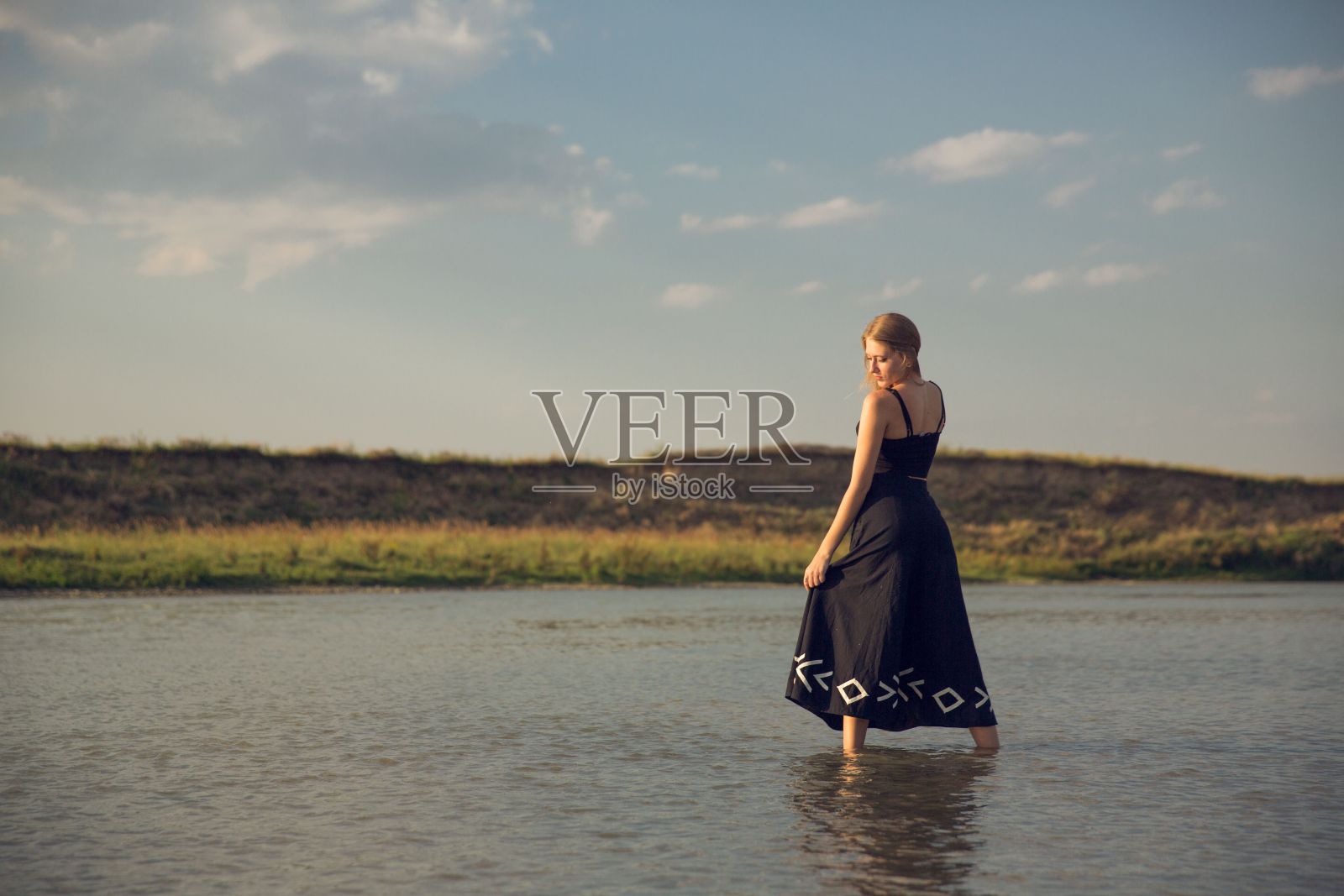 金发性感的女性在海边日落黑色连衣裙照片摄影图片