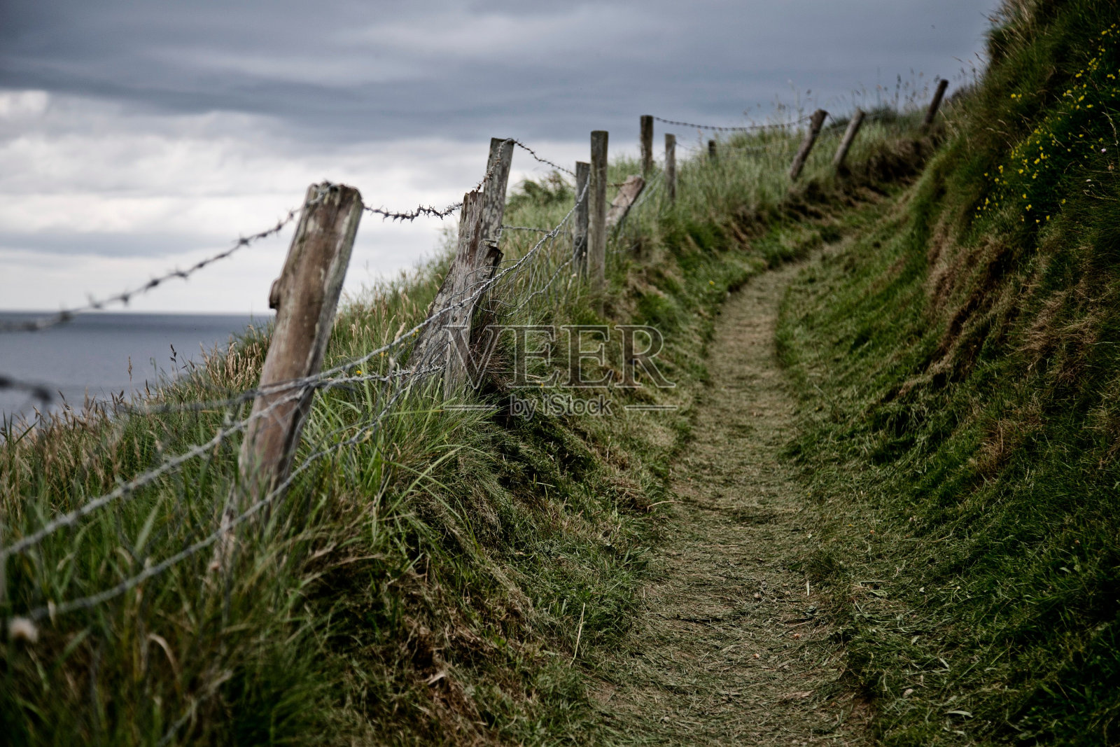 山坡上的道路,边缘的木头上有铁丝网,背景是爱尔兰海照片摄影图片