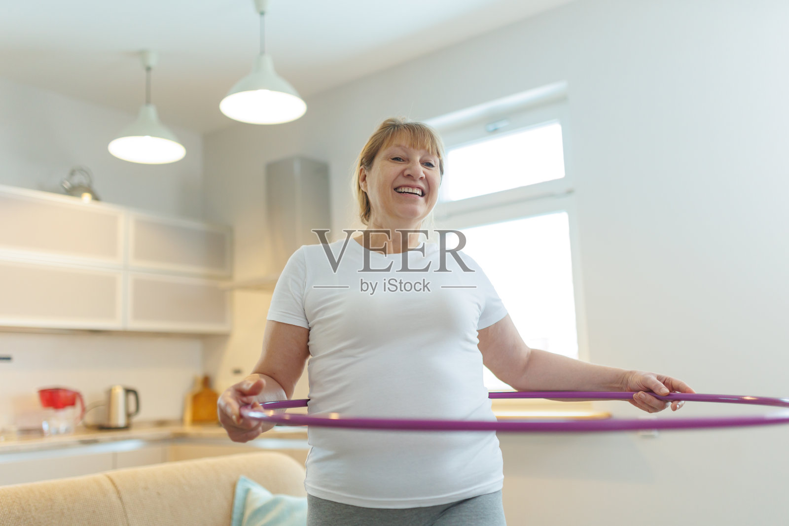 穿着白色t恤和灰色紧身裤的超重成熟女子试图用呼啦圈练习减肥照片摄影图片