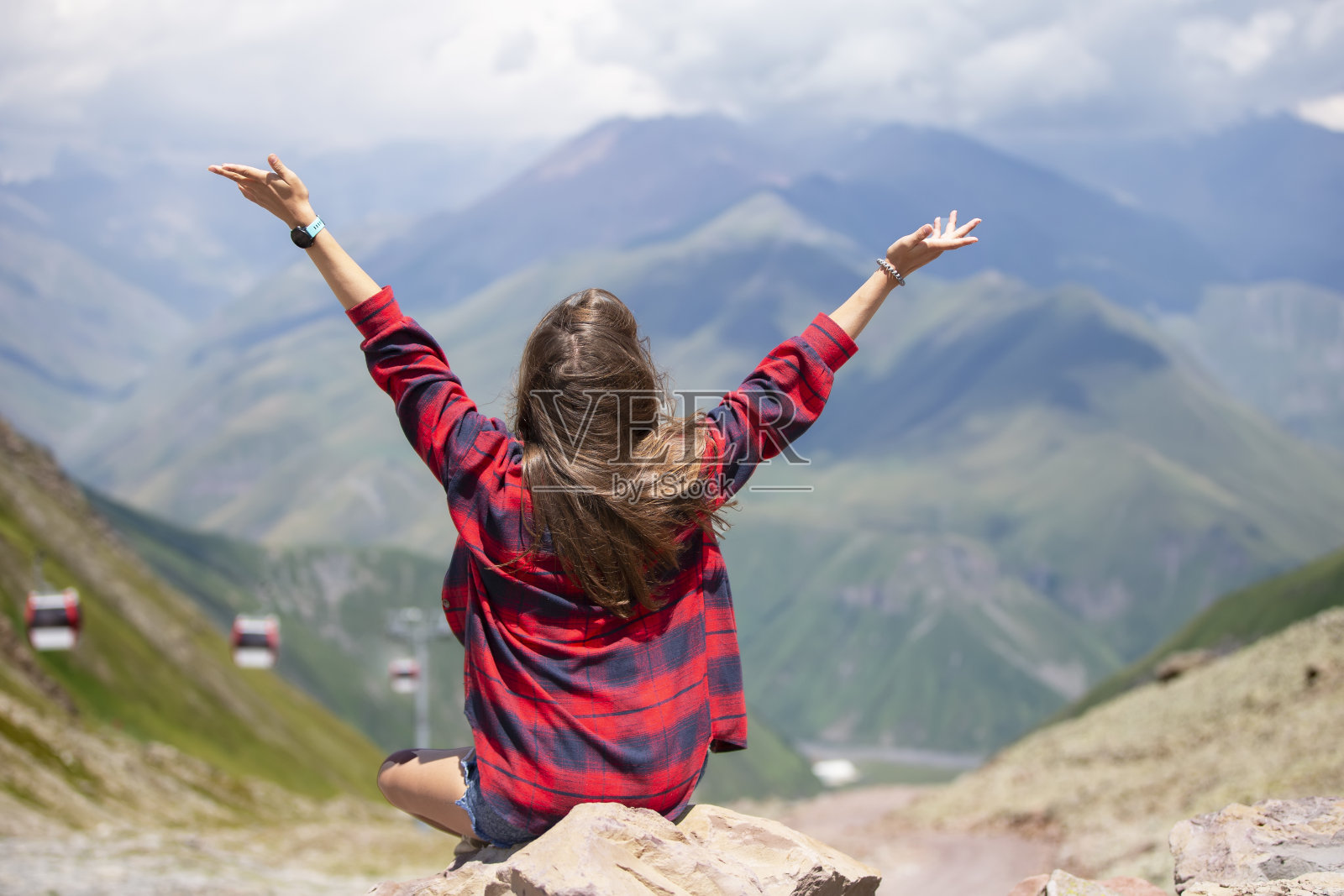 快乐的女游客在山顶上举起双手,欣赏着美丽的山景。照片摄影图片