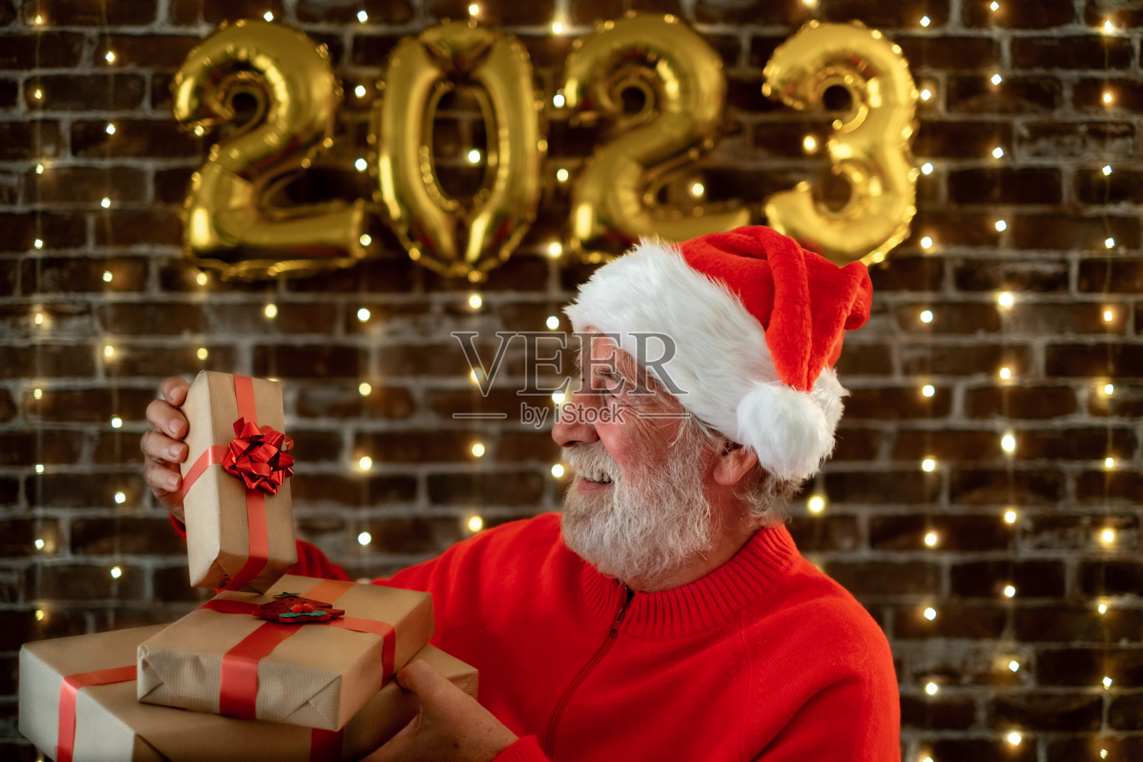 庆祝新年活动,白人络腮胡老人拿着圣诞礼物——漂亮的年长男人戴着圣诞帽在晚上在家庆祝节日照片摄影图片