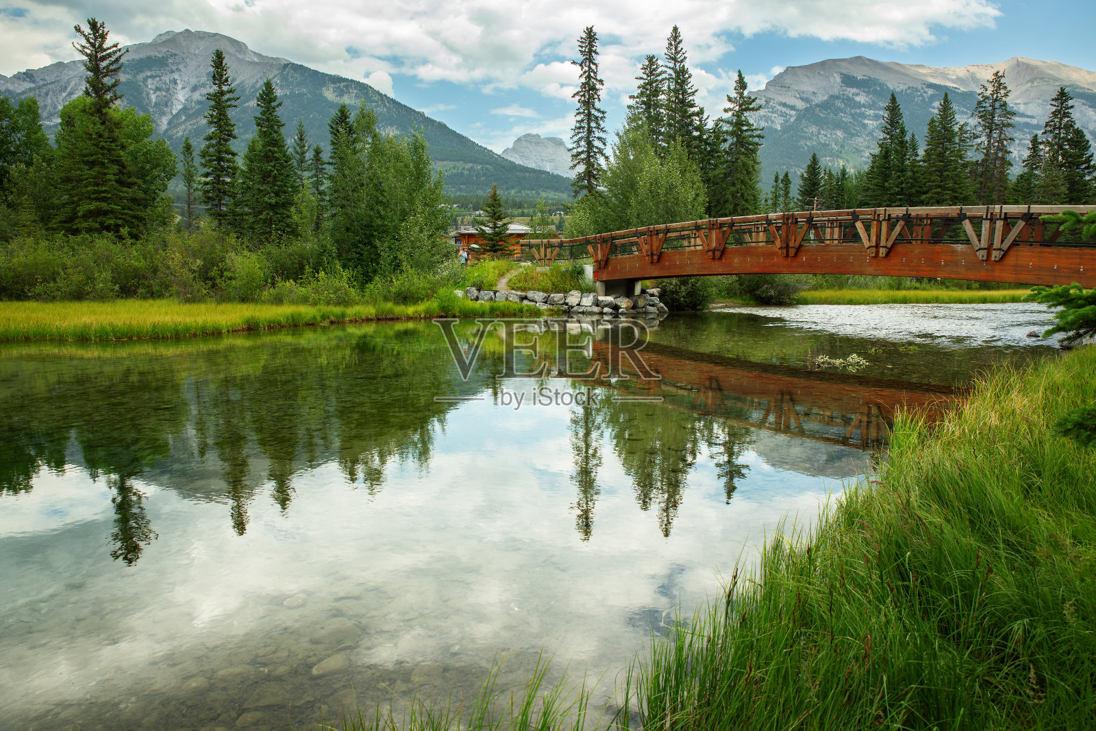 宁静的河流上有一座桥,周围是绿色植物,背后是群山照片摄影图片