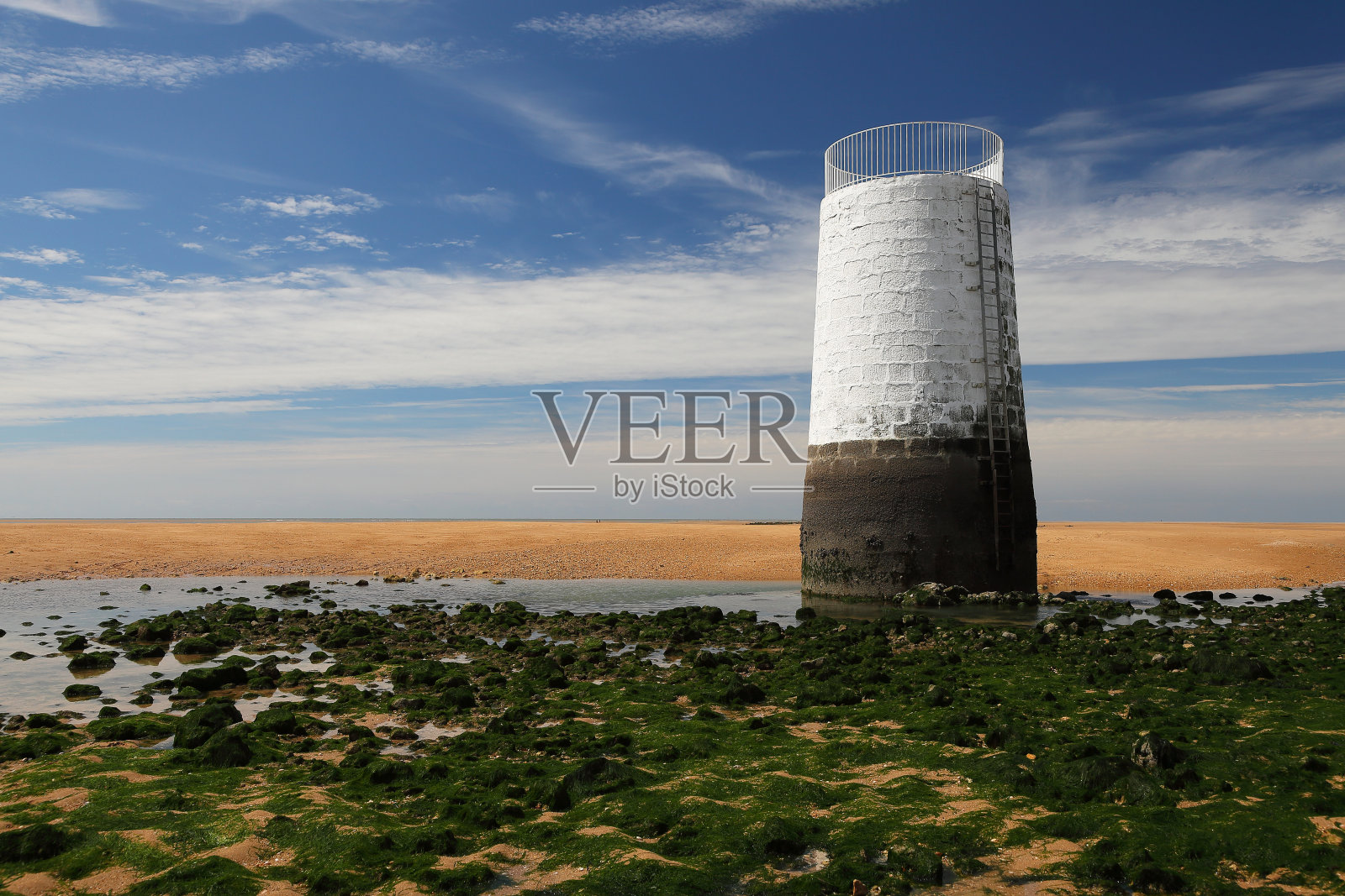 退潮时的沙滩,岩石上覆盖着海藻和白色的塔照片摄影图片