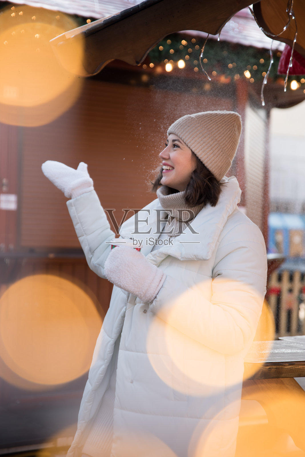 公平的。女孩穿着白夹克,戴着白帽子。女孩笑了。手里拿着一杯咖啡。木制避暑别墅。女孩喜悦。的情绪。照片摄影图片