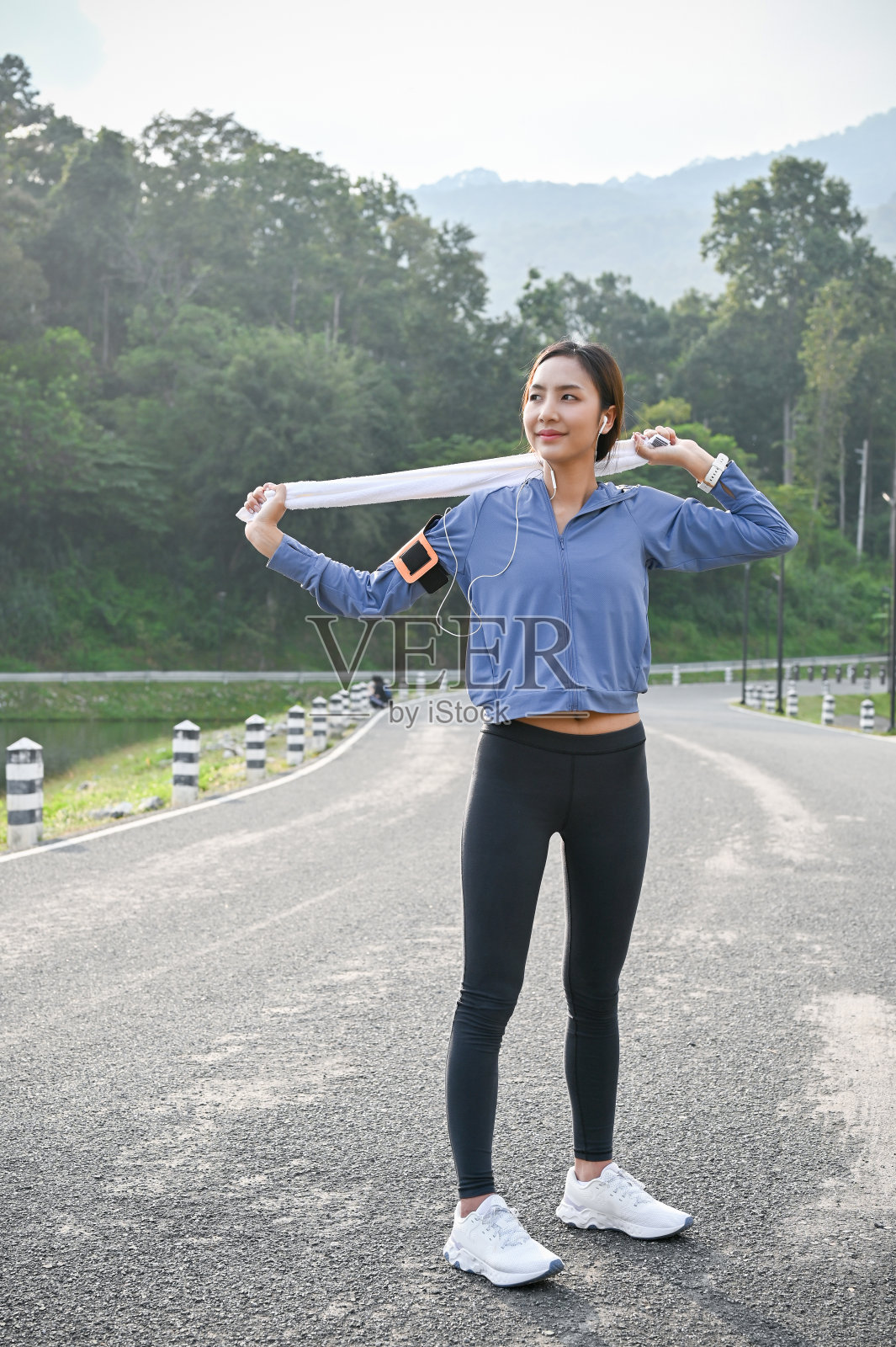 一个迷人的亚洲女人站在街上,拿着毛巾,戴着耳机听音乐。照片摄影图片