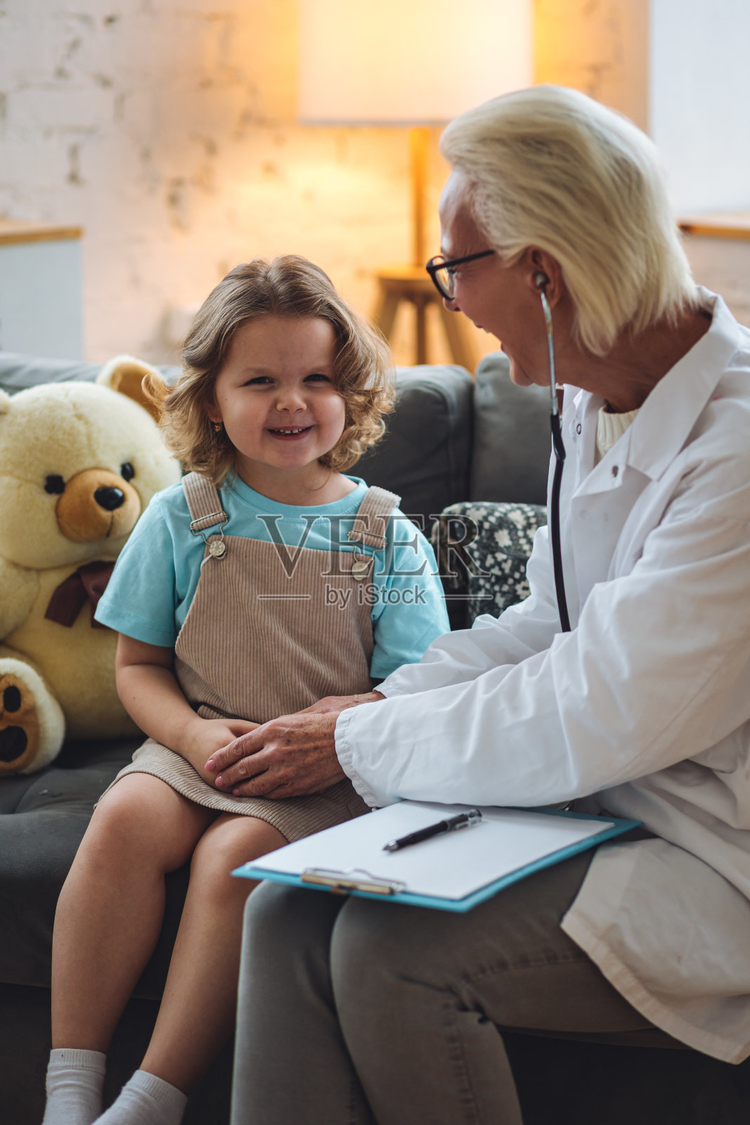 善良的女老年儿科医生到家里看望他的病人,检查小女孩,写处方。儿童健康检查的概念测量体温,心跳照片摄影图片