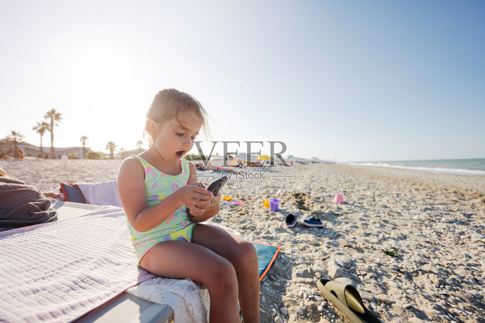 意大利波尔图圣埃尔皮迪奥海滩上,女婴坐着玩手机。照片摄影图片